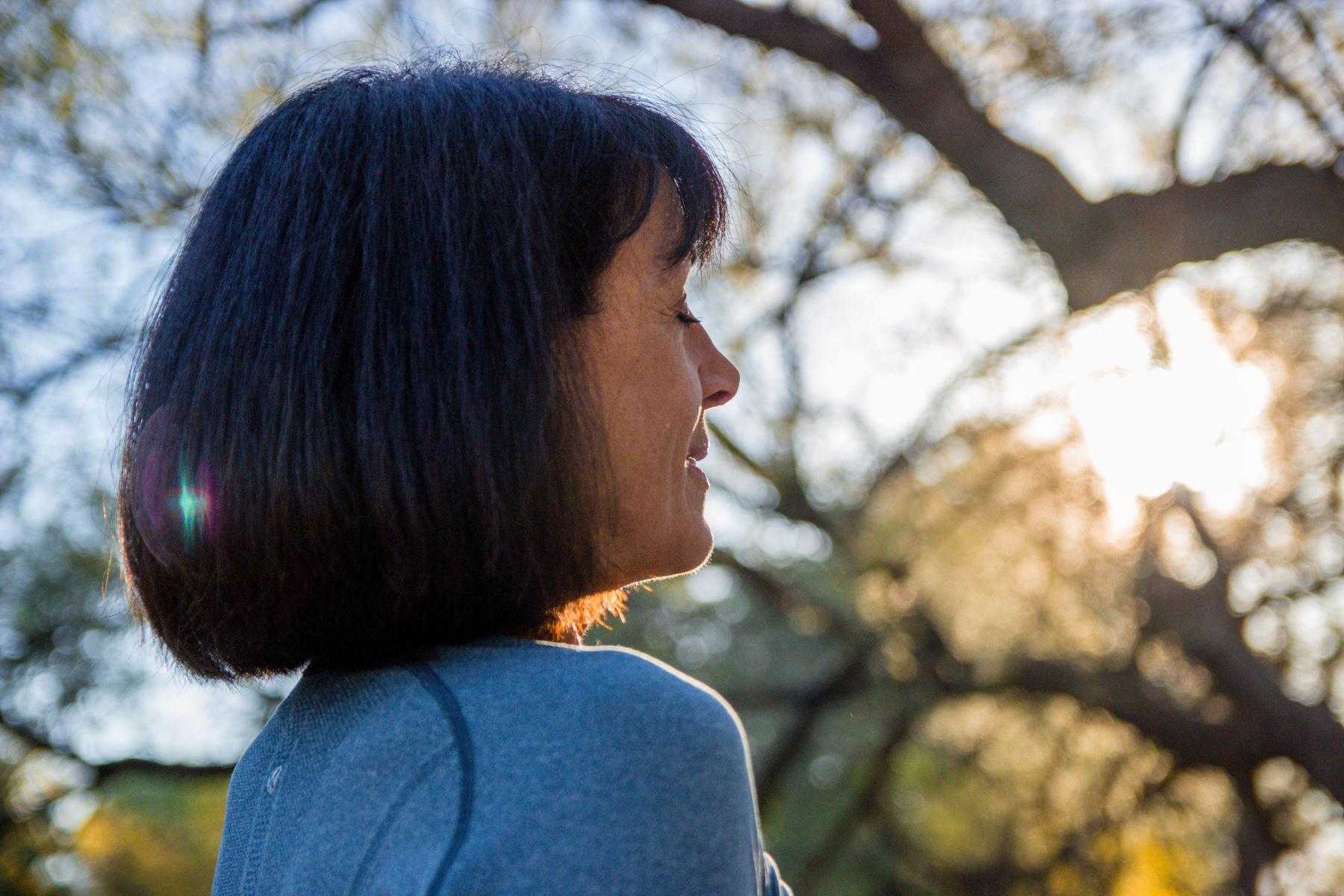 A woman standing in a wooded area looking off into the distance.