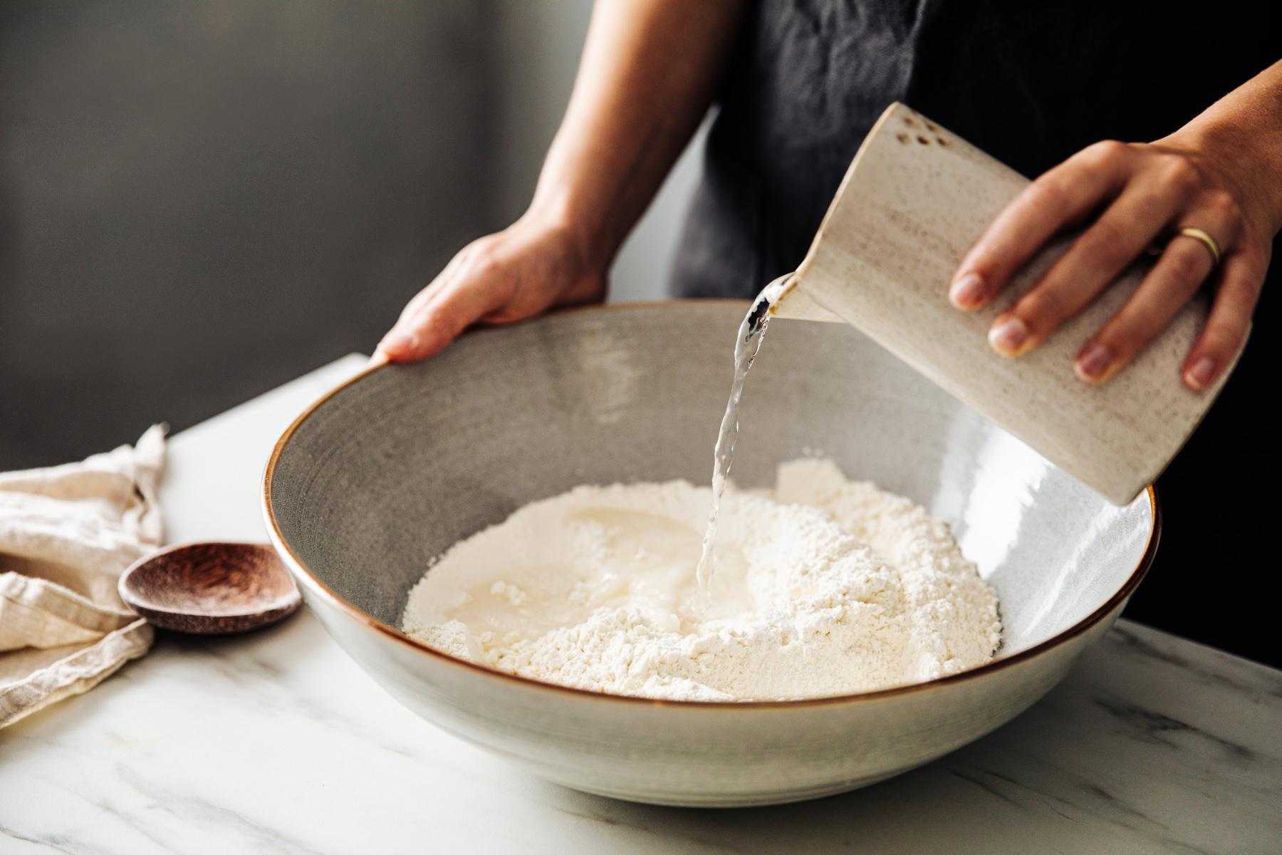 woman pouring water into bowl of flour to make bread