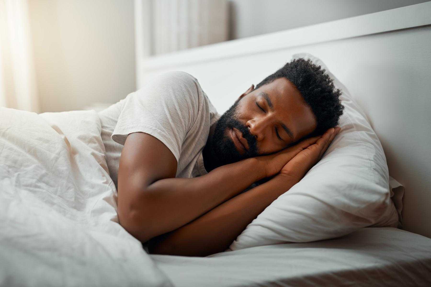 Man laying on his side in a bed with hands tucked up under the side of face.