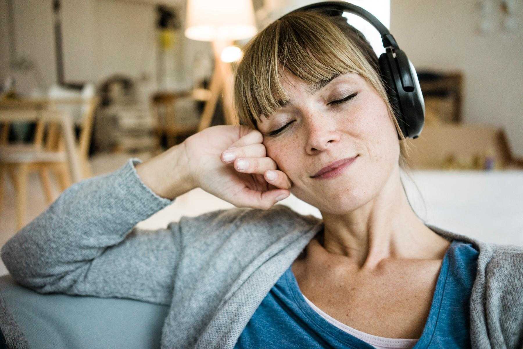 Woman sitting on her couch with headphones on listening to music.