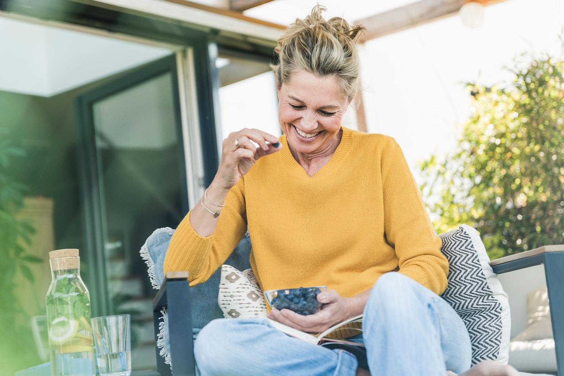 Woman smiling while eating blueberries outside.