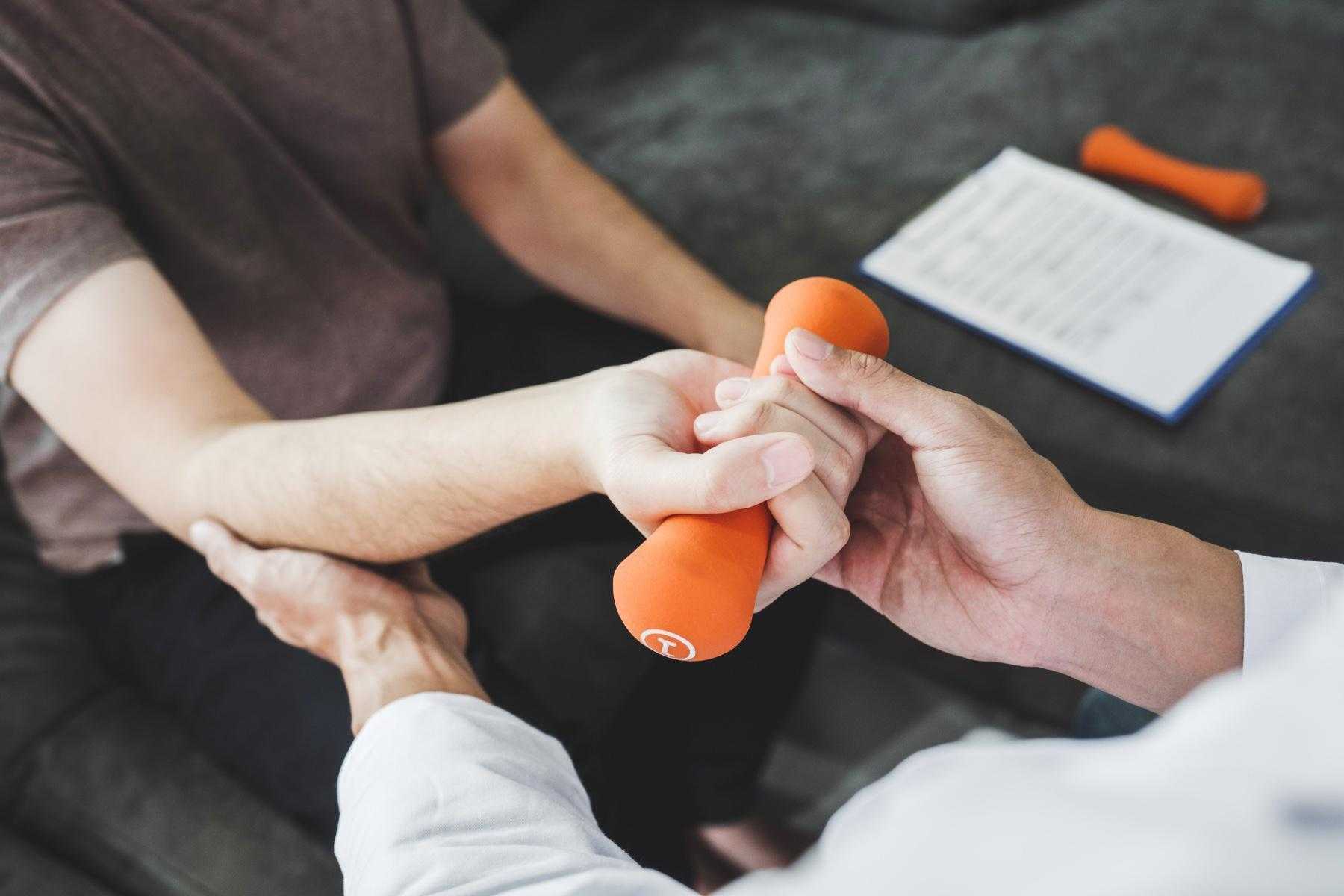 Close-up on man receiving assistance from a physical therapist as he curls a 1 pound orange dumbbell.