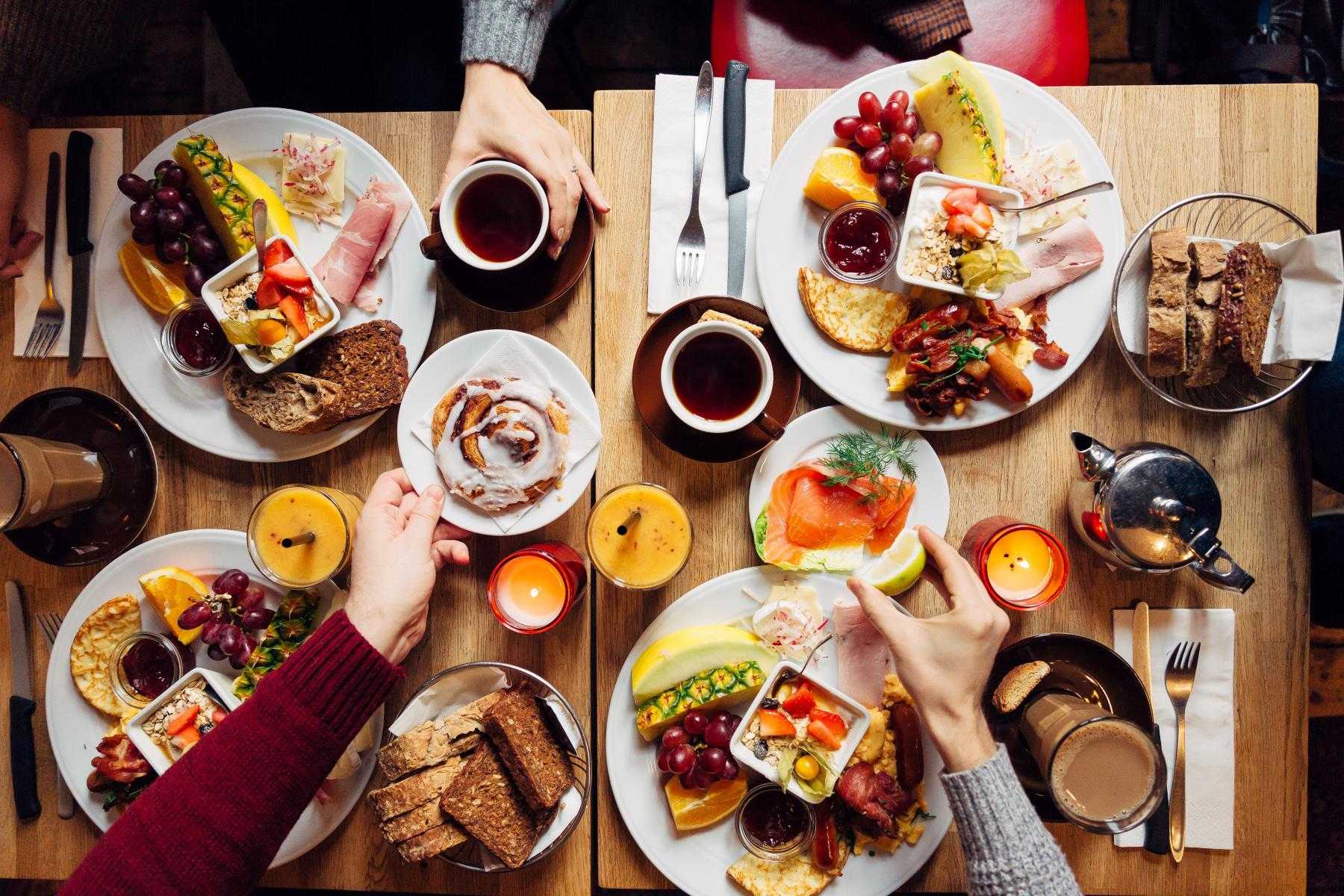 overhead image of four hands reaching out over food-filled dinner table