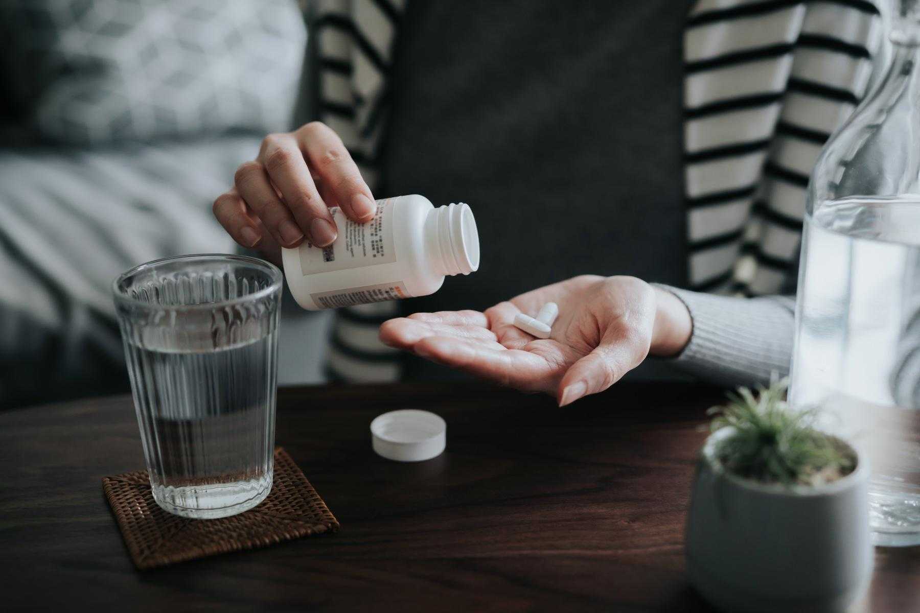 Close-up of woman pouring supplements out of bottle into her hand.