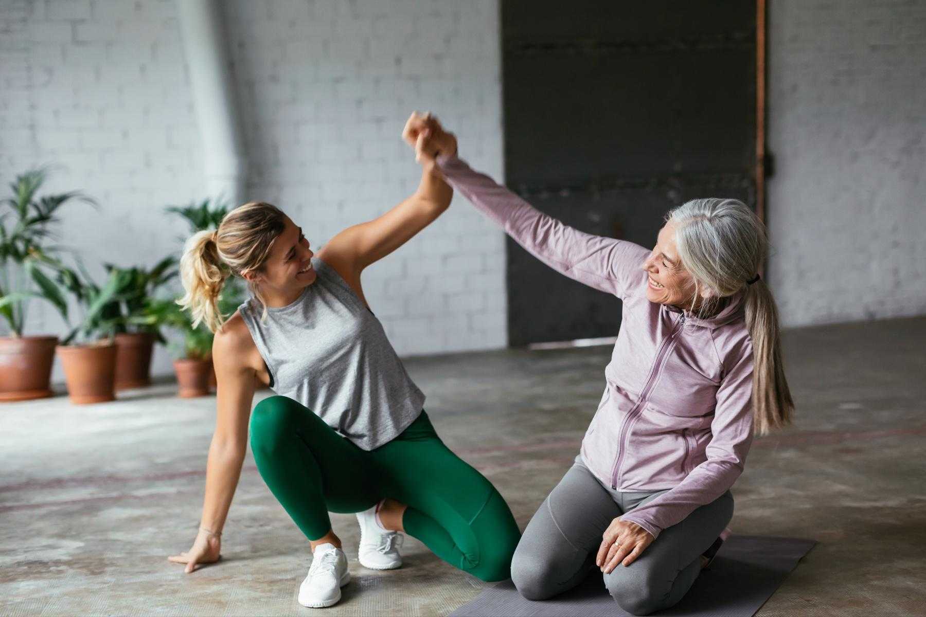 two women mid workout kneeling on the ground and holding their hands together in the air in celebration