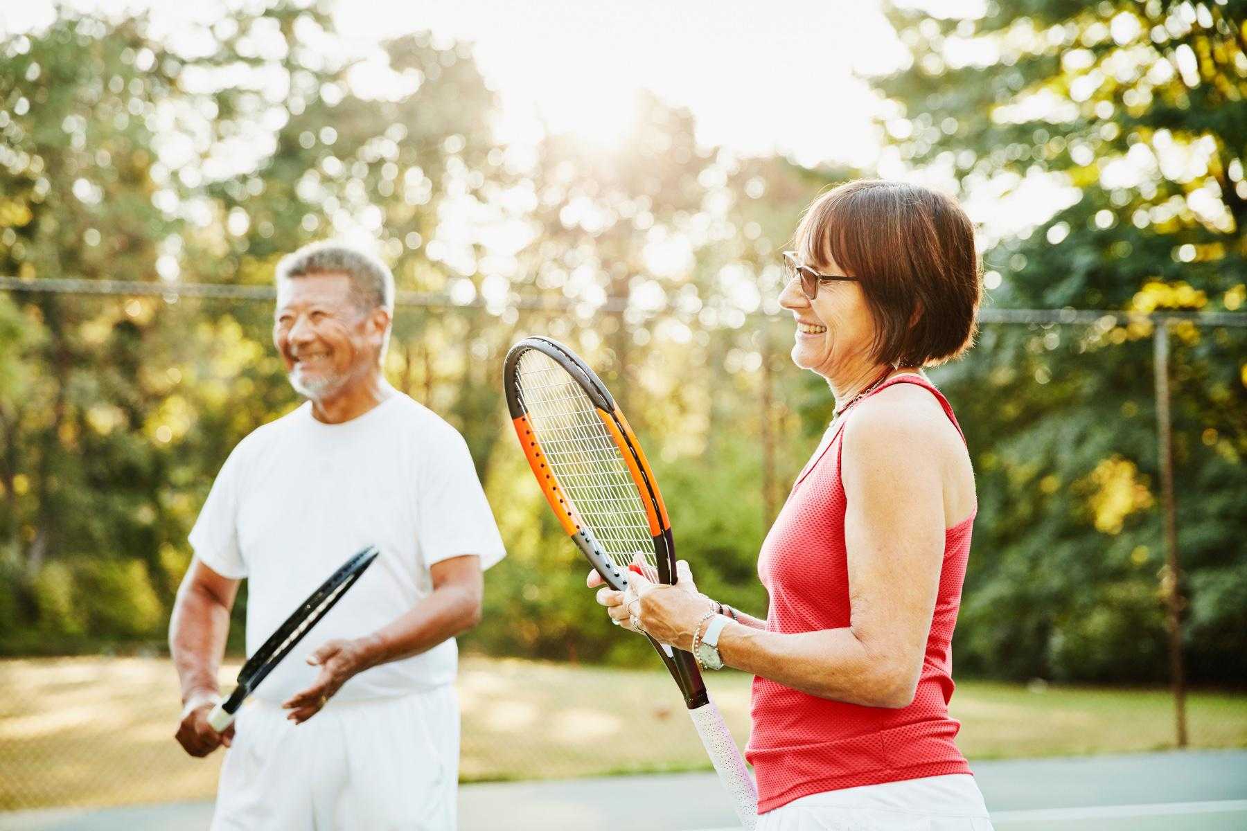 man and woman smiling outside with tennis rackets as they stand in tennis court