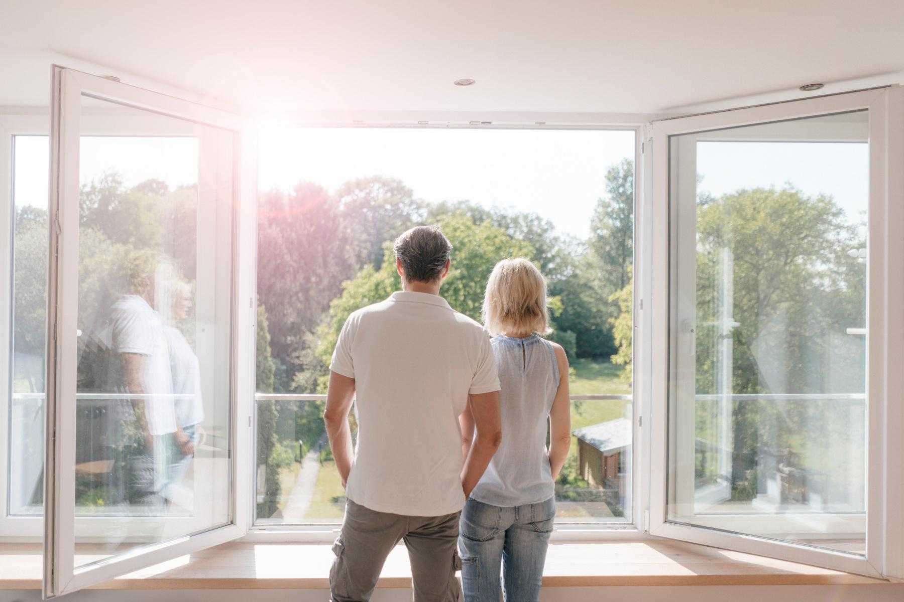 A couple looking outside of a large window at trees.