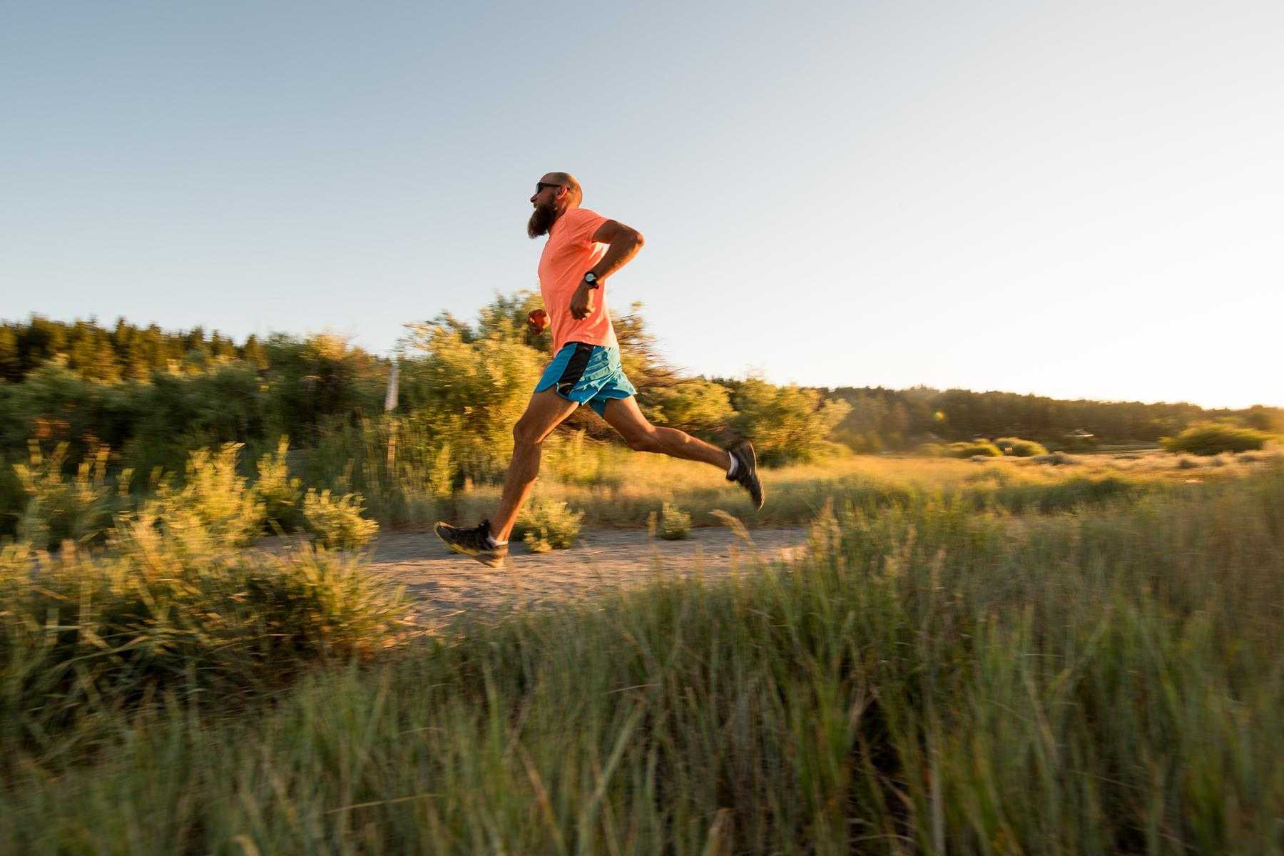 Side view of man running outside on trail on sunny day.