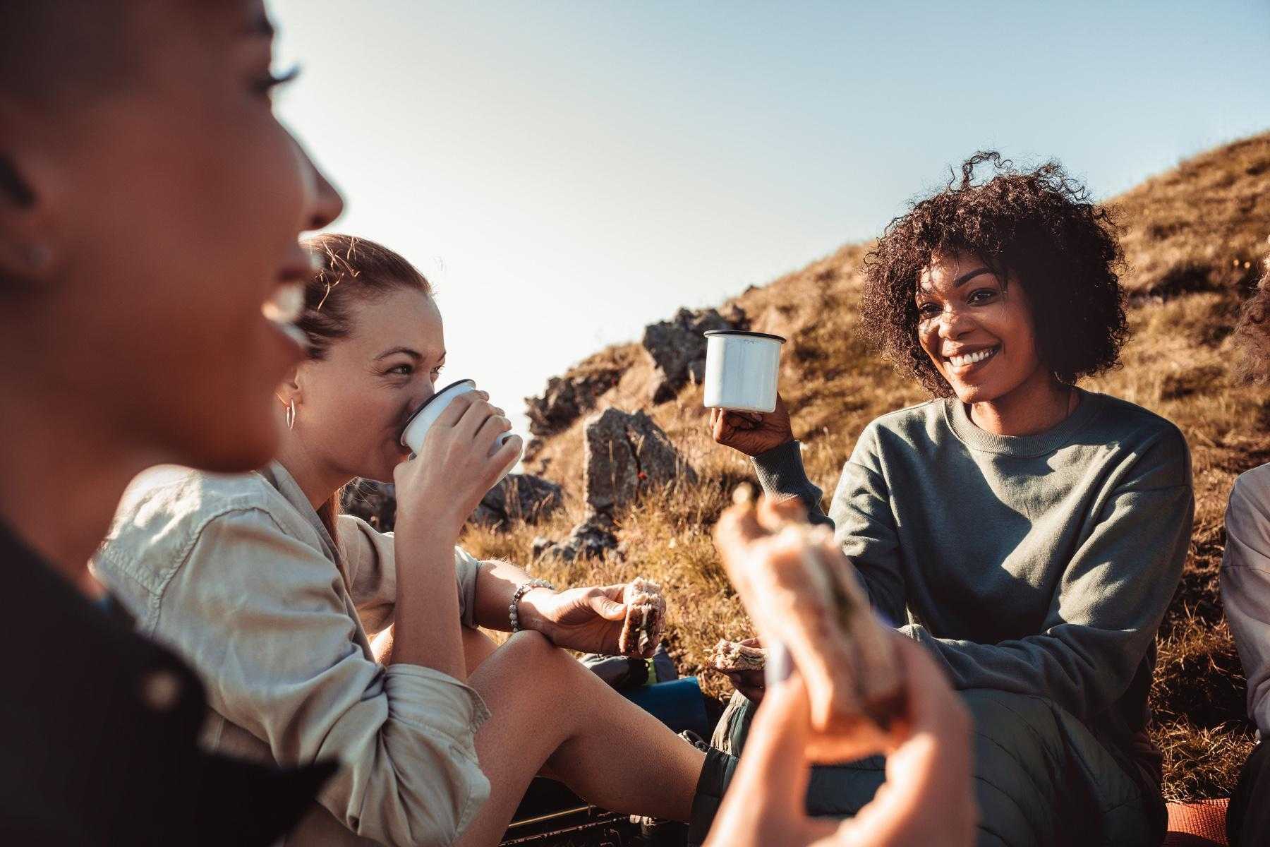 Three women sitting on mountain top drinking coffee.