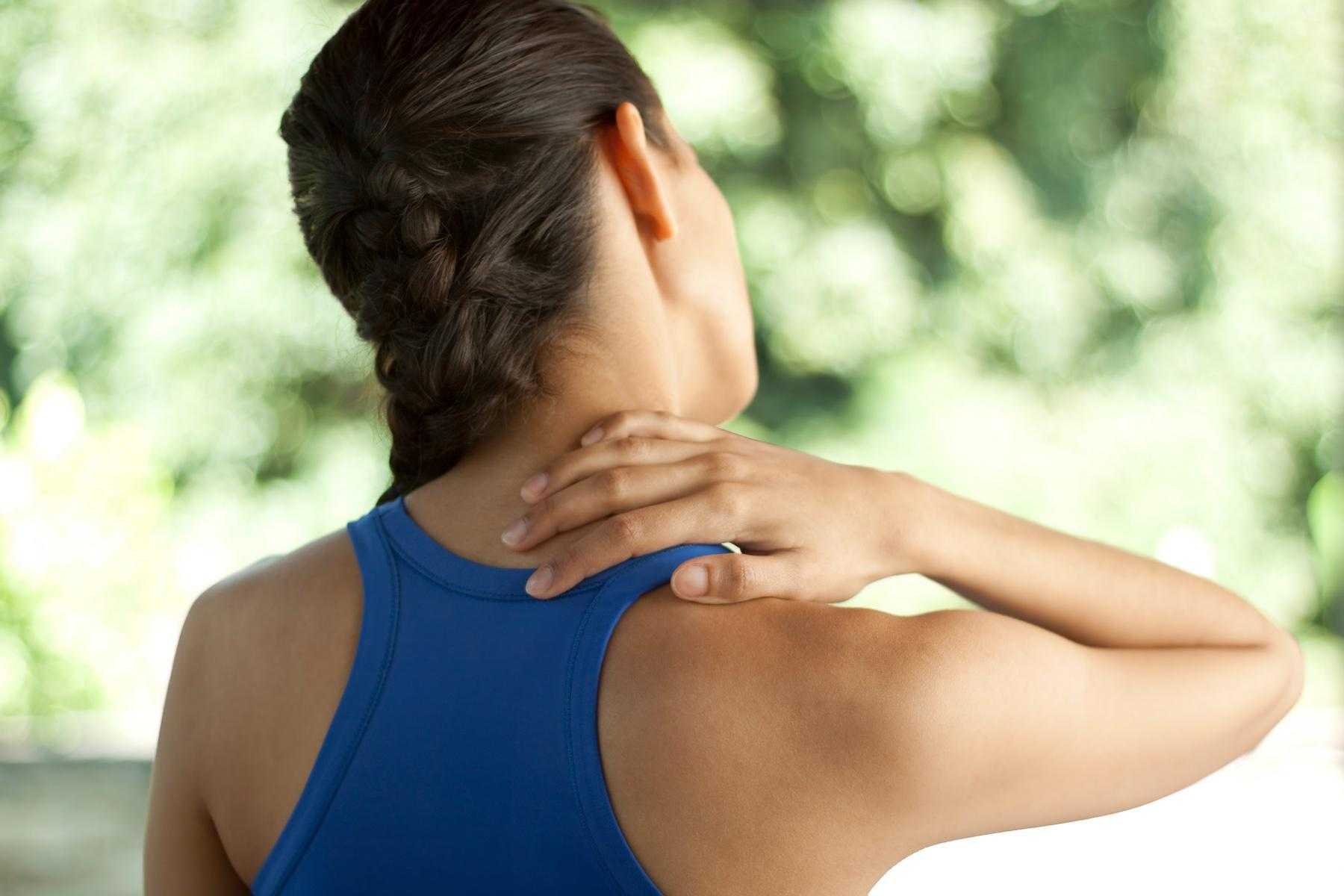 close-up of woman's back as she grabs her neck in pain