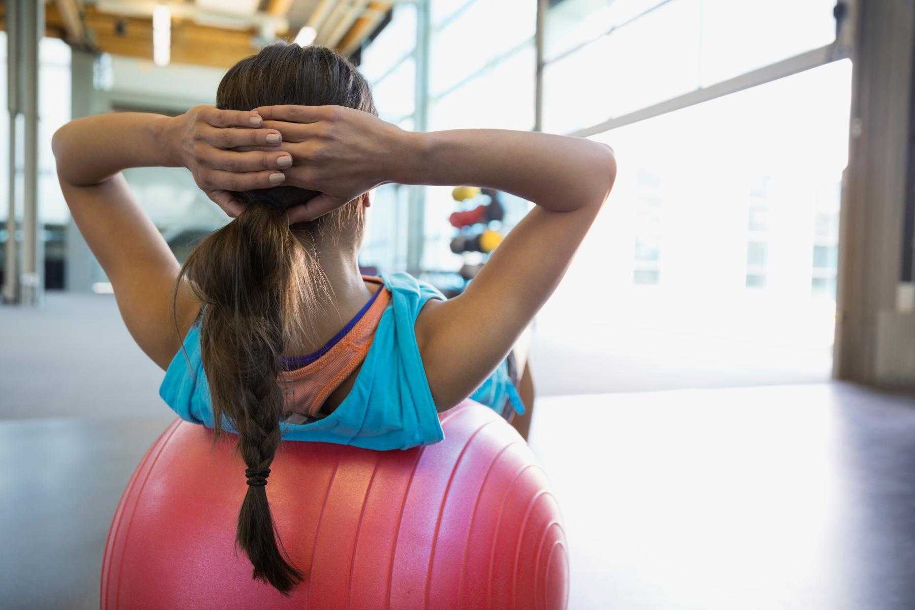 up-close of woman's back as she does a crunch on a workout ball with her hands on her head