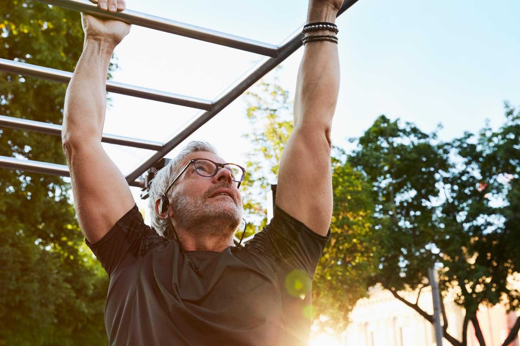 Older man climbing on outdoor fitness equipment.