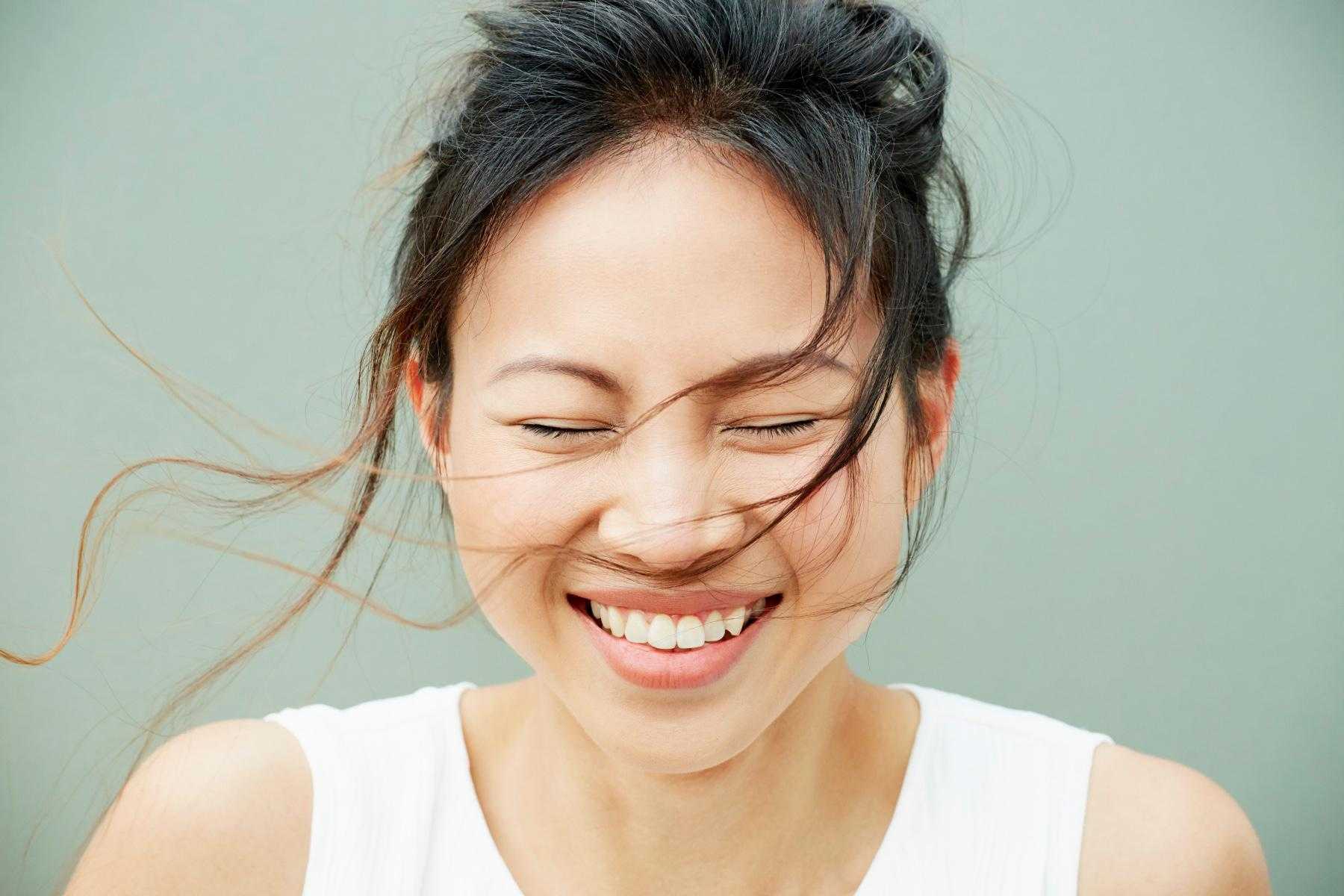 A close-up of a woman smiling with her eyes closed as the wind blows her hair into her face.