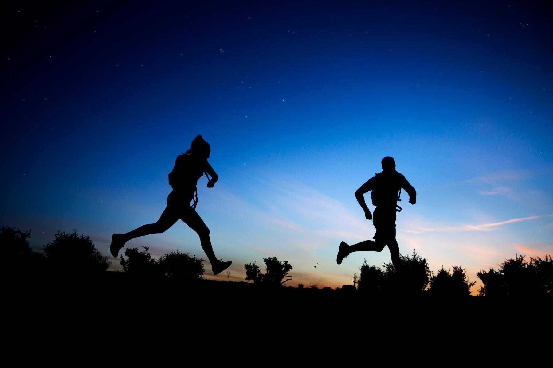 Man and woman silhouetted as they run against a background of stars and sunset in the Sonoran Desert.