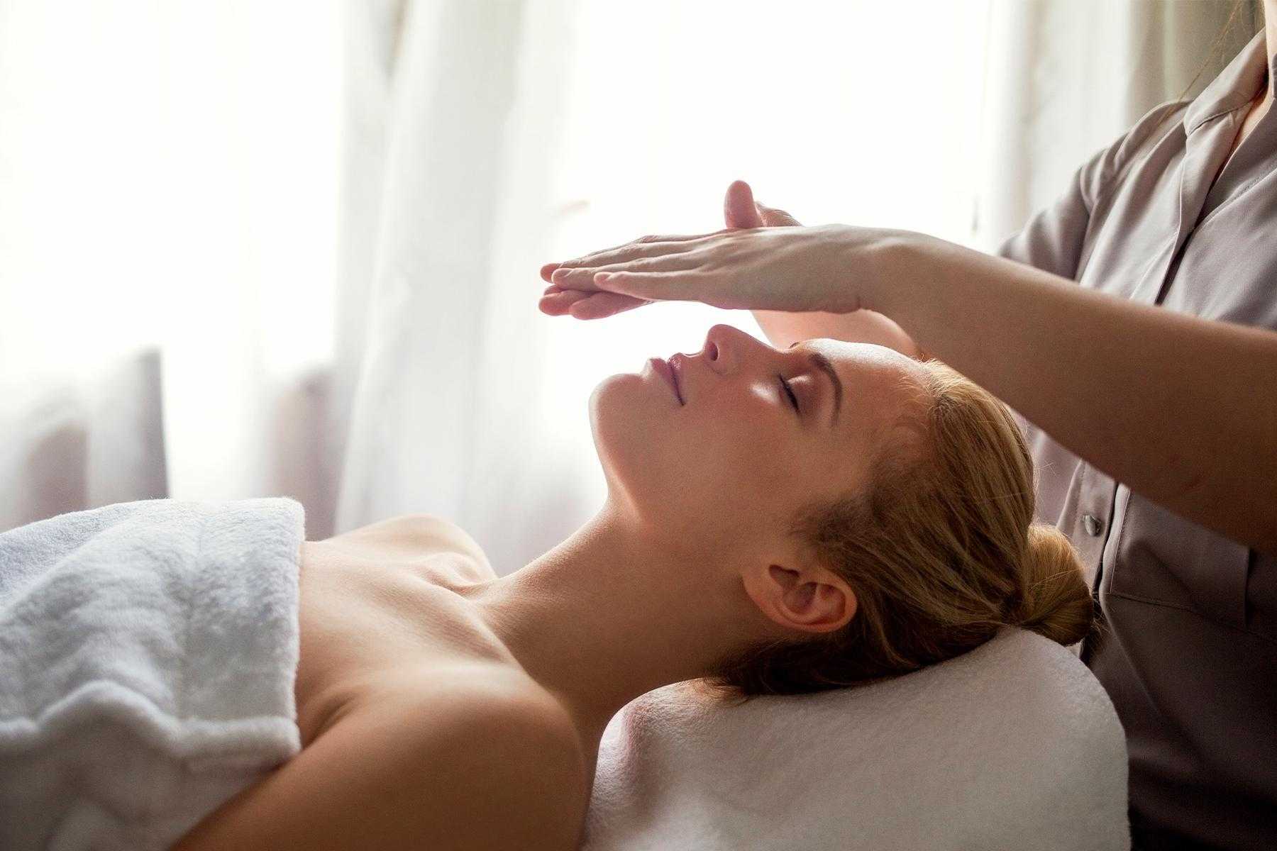 Woman laying on massage table with practitioner's hands above her face during a healing energy treatment.