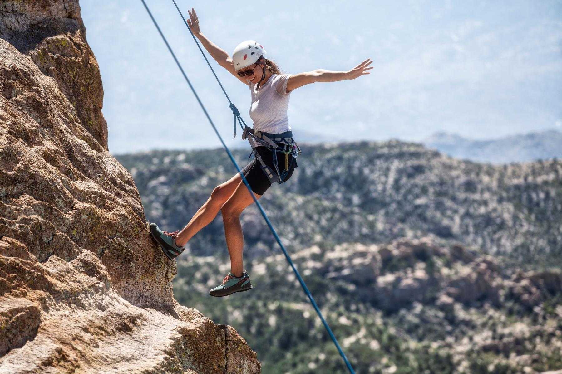 woman on side of rock face while rock climbing smiling while coming down