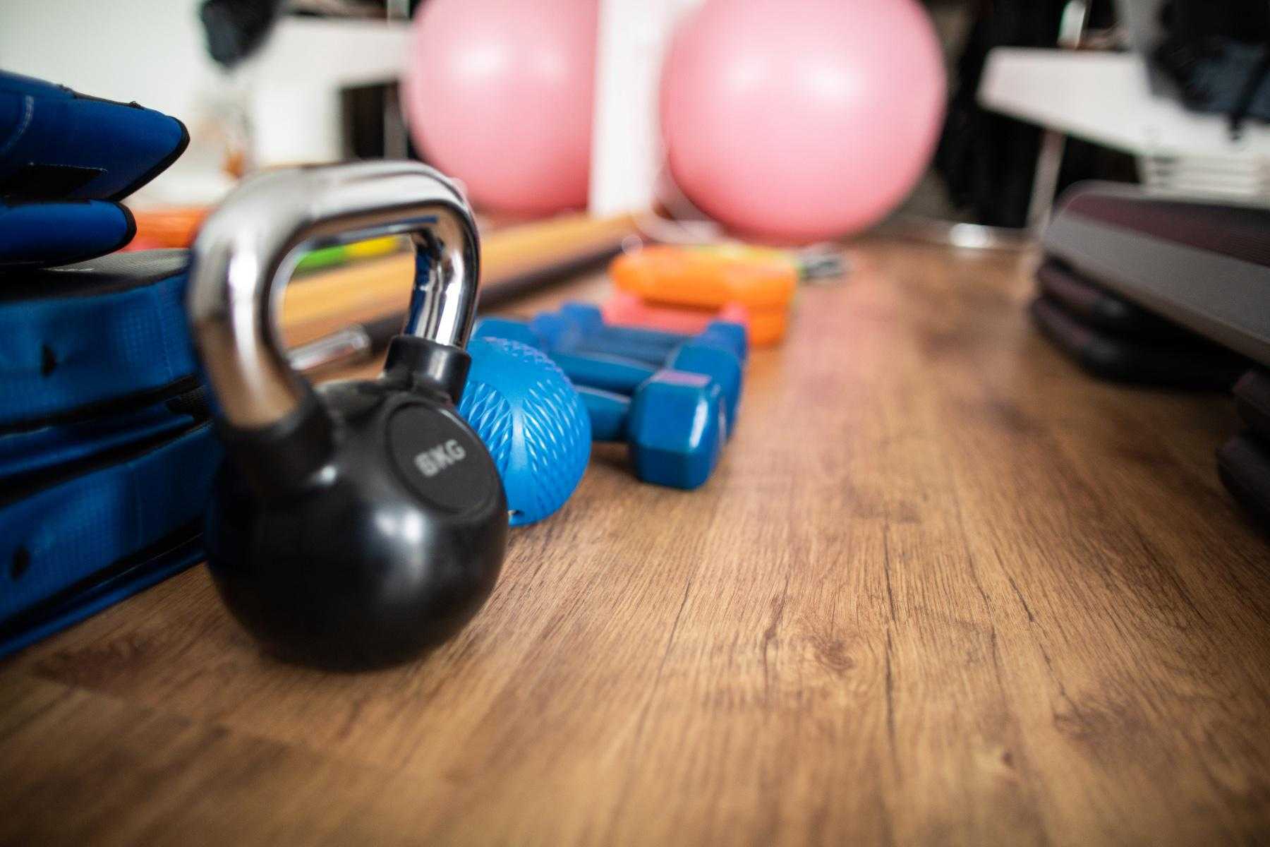 close-up of row of home fitness equipment including a kettlebell, a large fitness ball, and small dumbbells