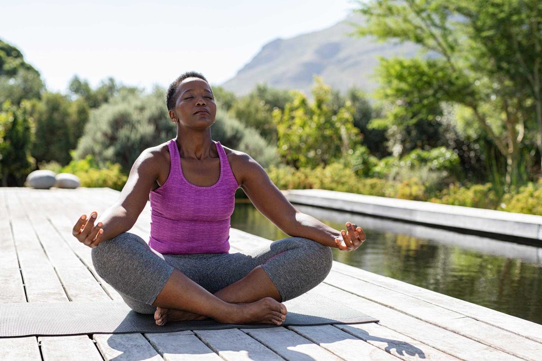 Woman meditating while sitting on dock outside.