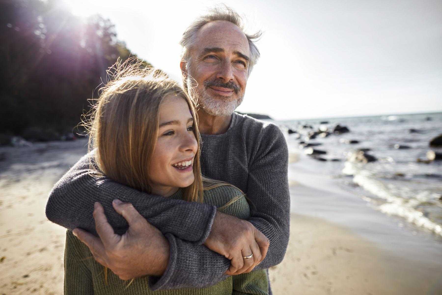A father and daughter at the beach hugging.