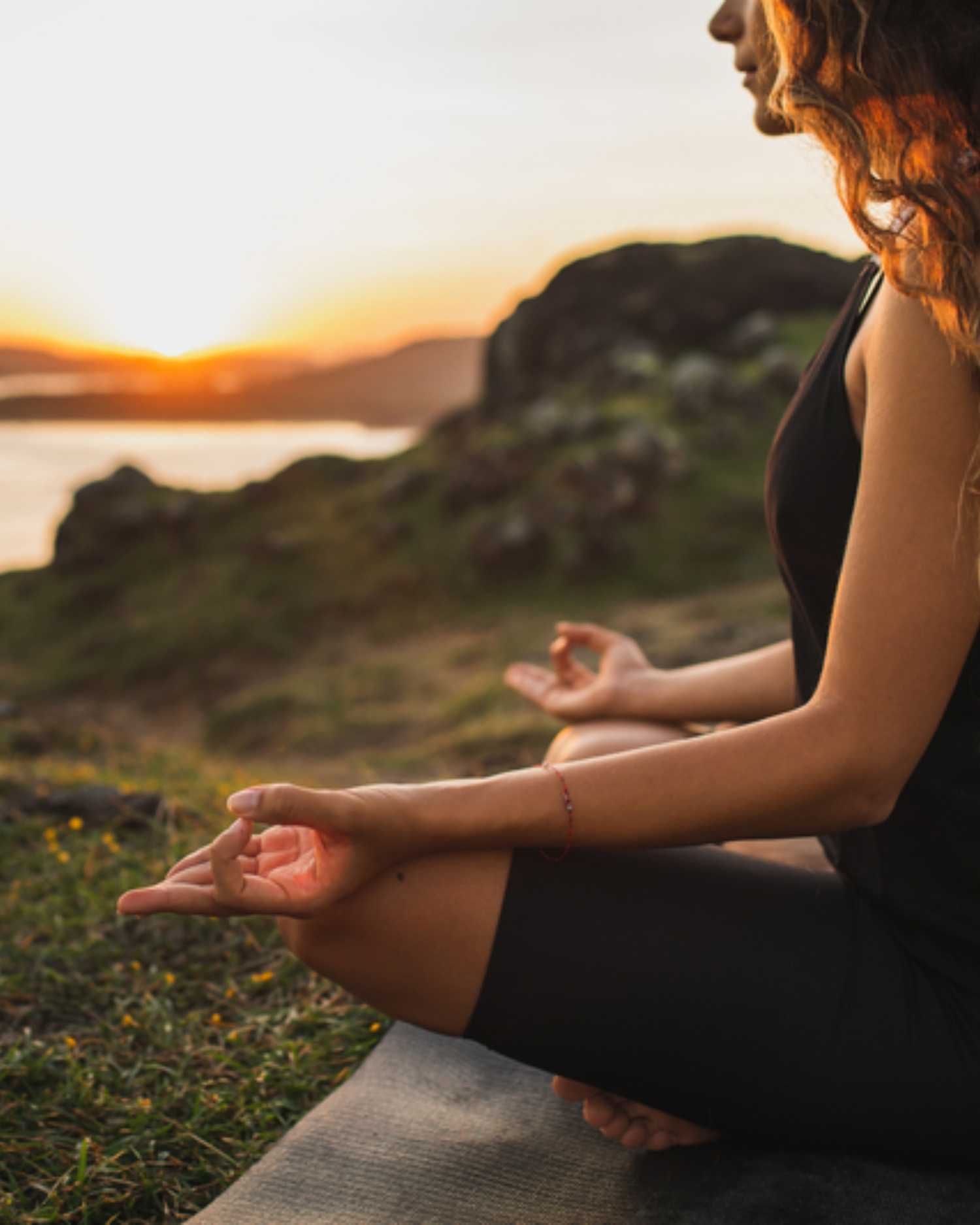 A woman meditating on a hill overlooking a lake