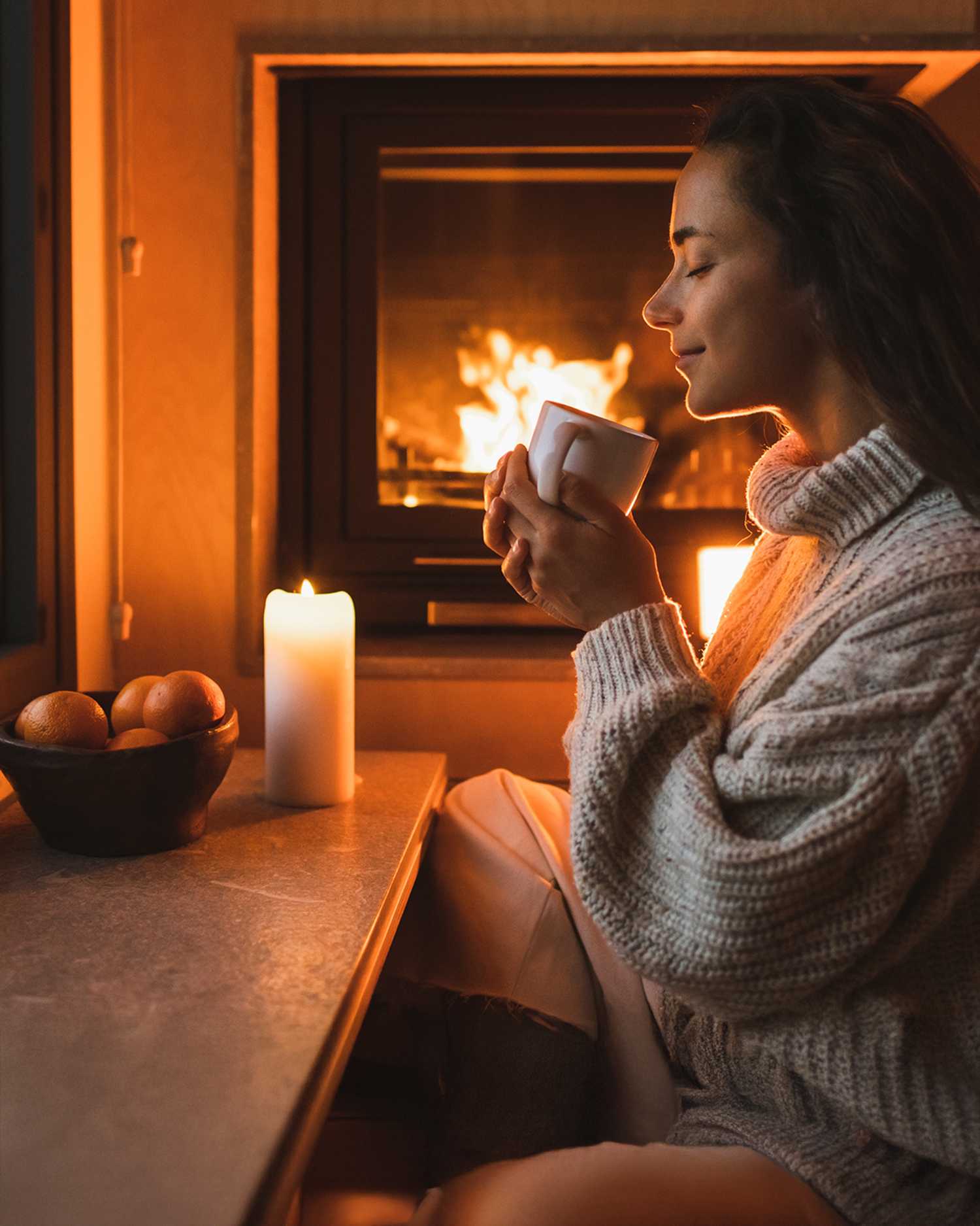 a woman enjoying the warmth of a fireplace and a hot drink