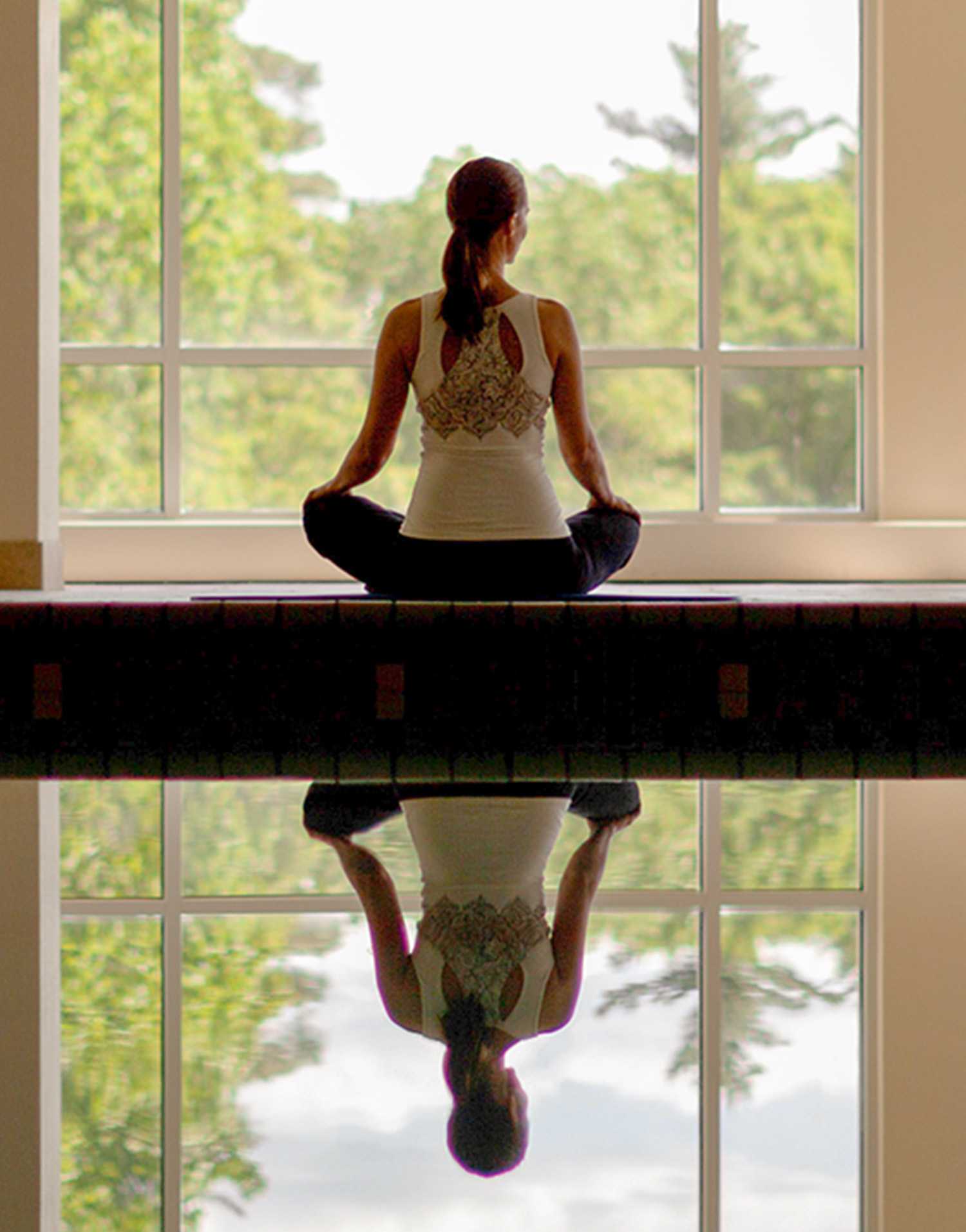 woman meditating in front of large windows