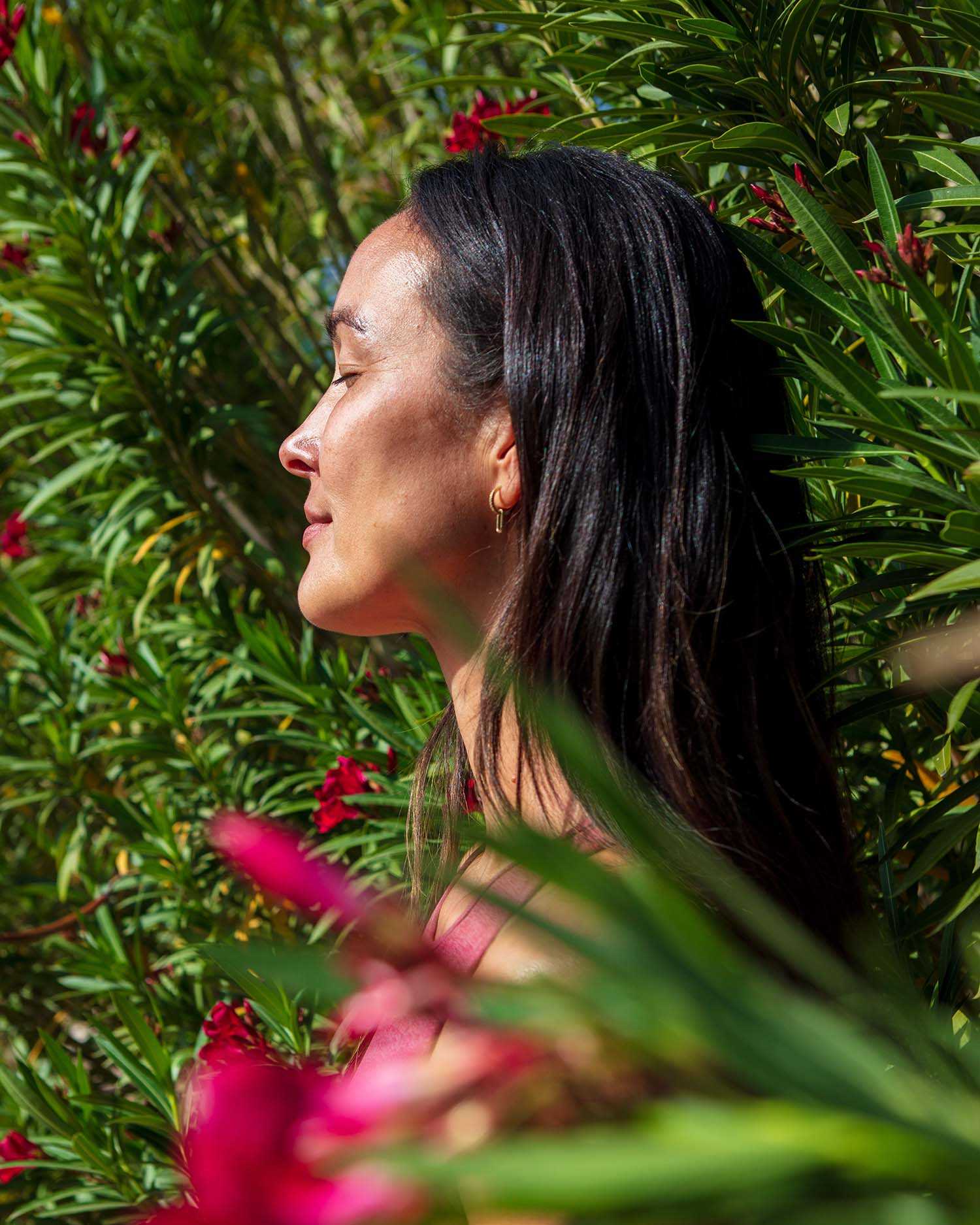Woman Standing With Closed Eyes Between Green Bushes and Pink Flowers 