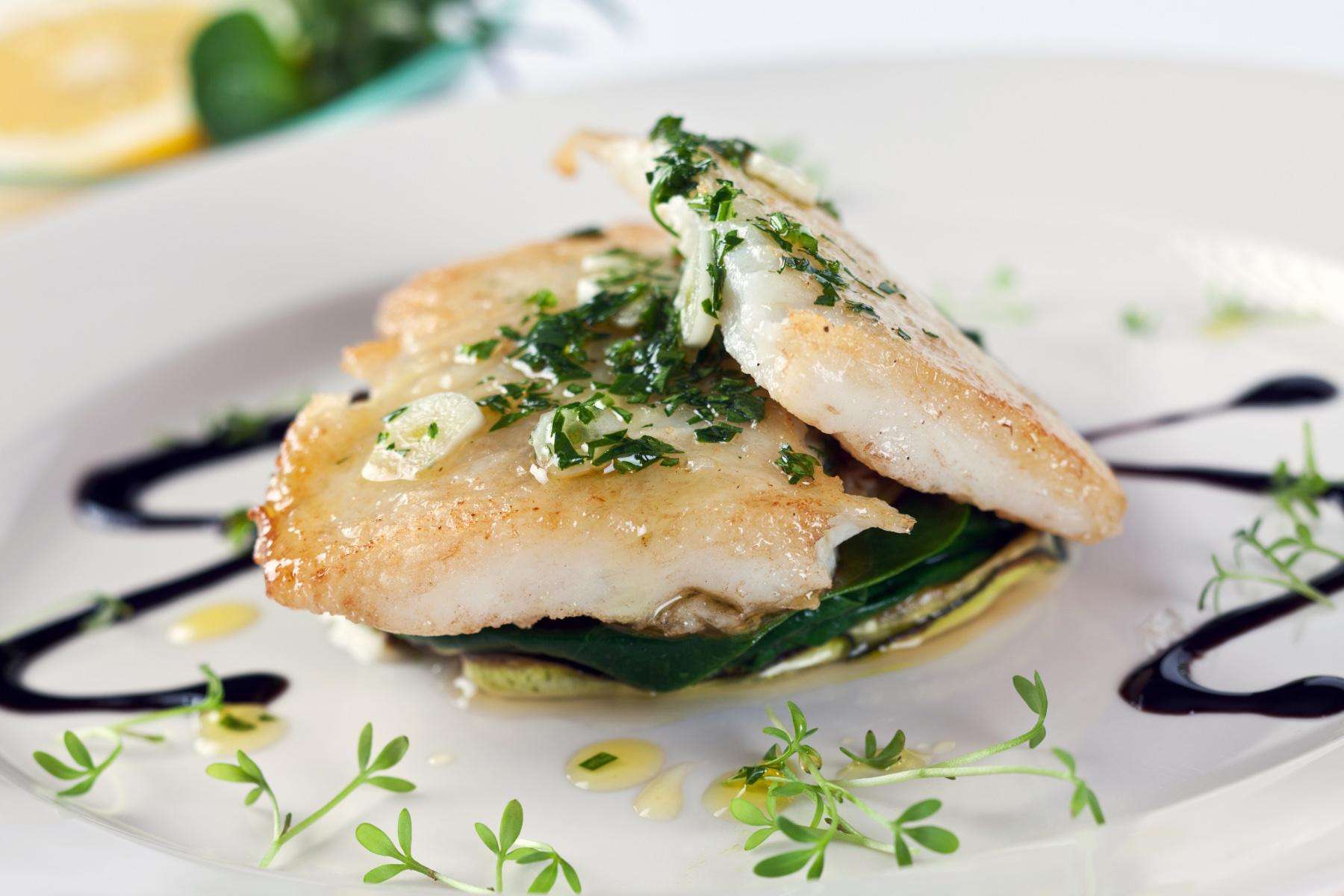 Cooked sole on plate with sauce drizzled around it.