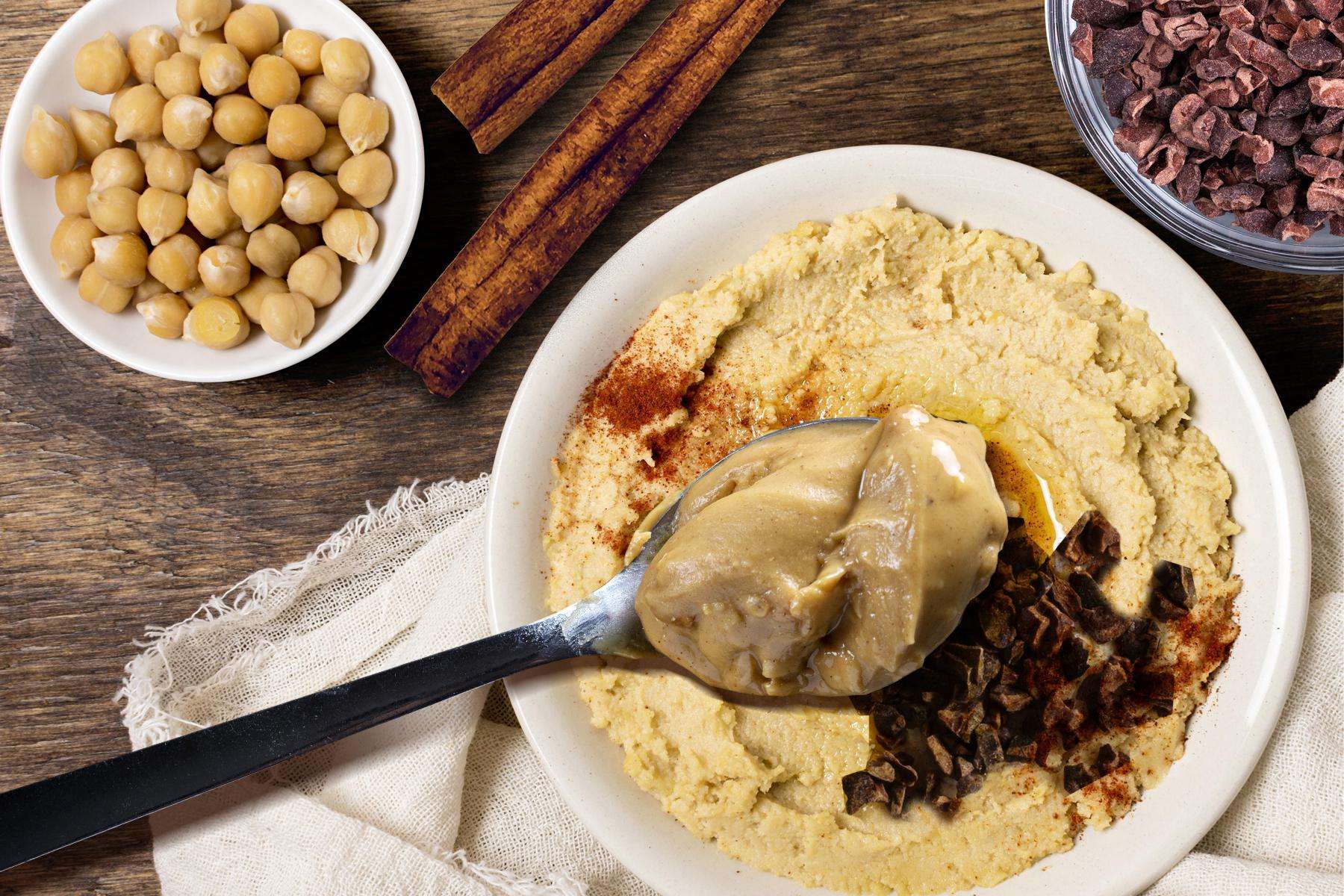 Overhead image of peanut butter hummus in bowl with ingredients surrounding it.