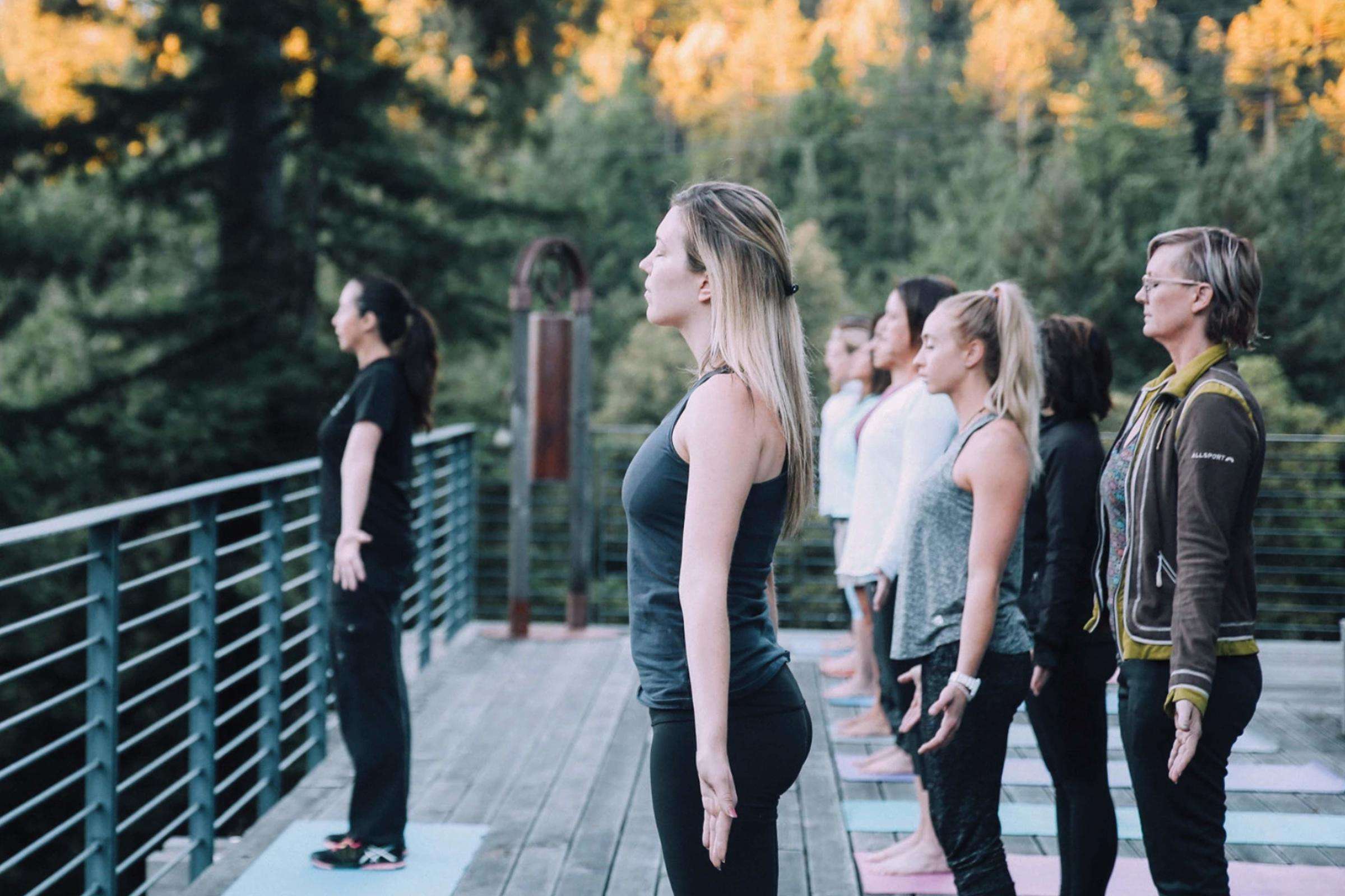group of women doing yoga outside on deck overlooking green pine trees