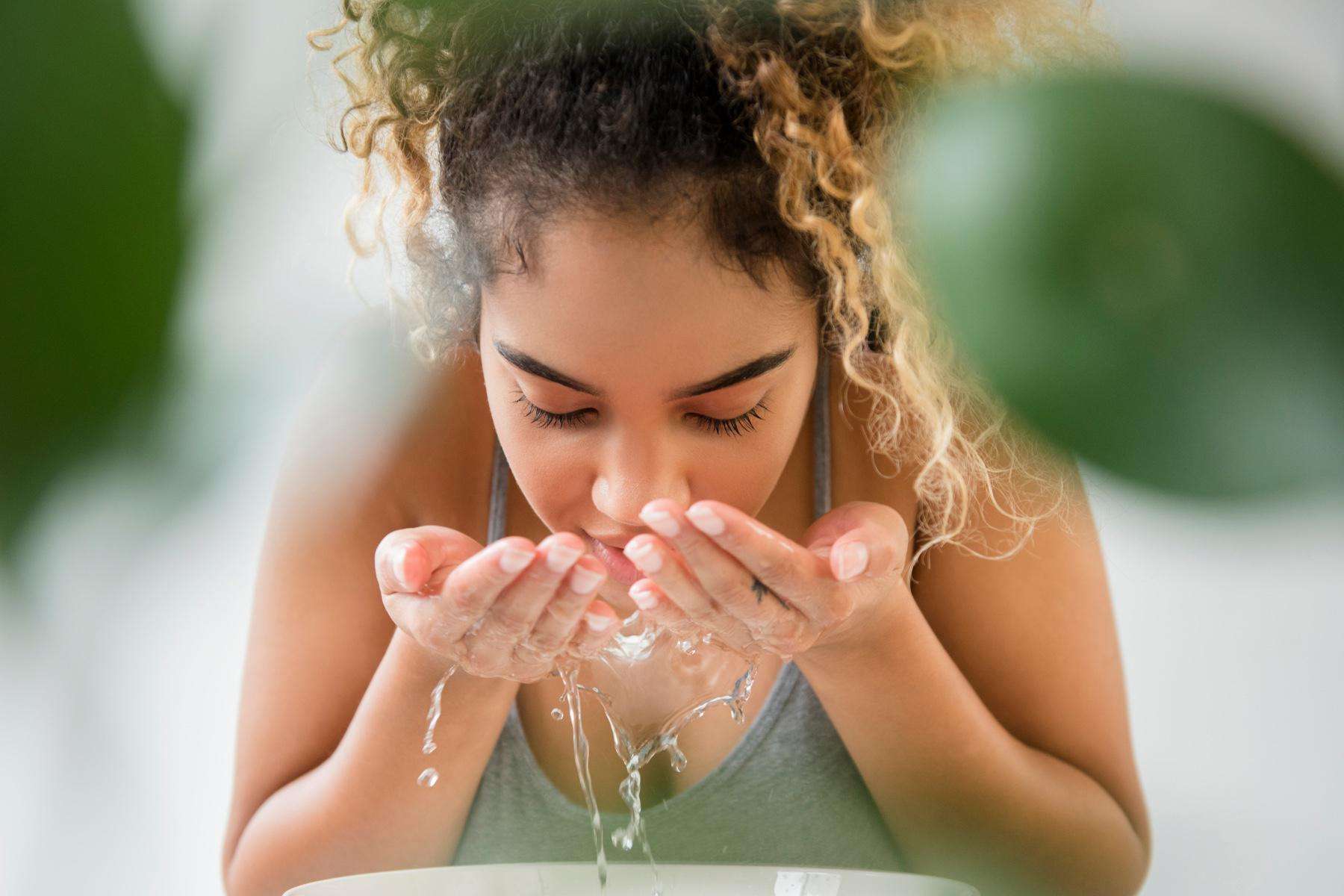 A young woman rinsing her face with water.