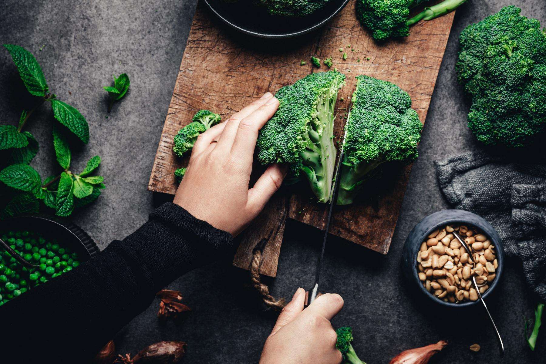 overhead shot of woman cutting broccoli on wooden cutting board