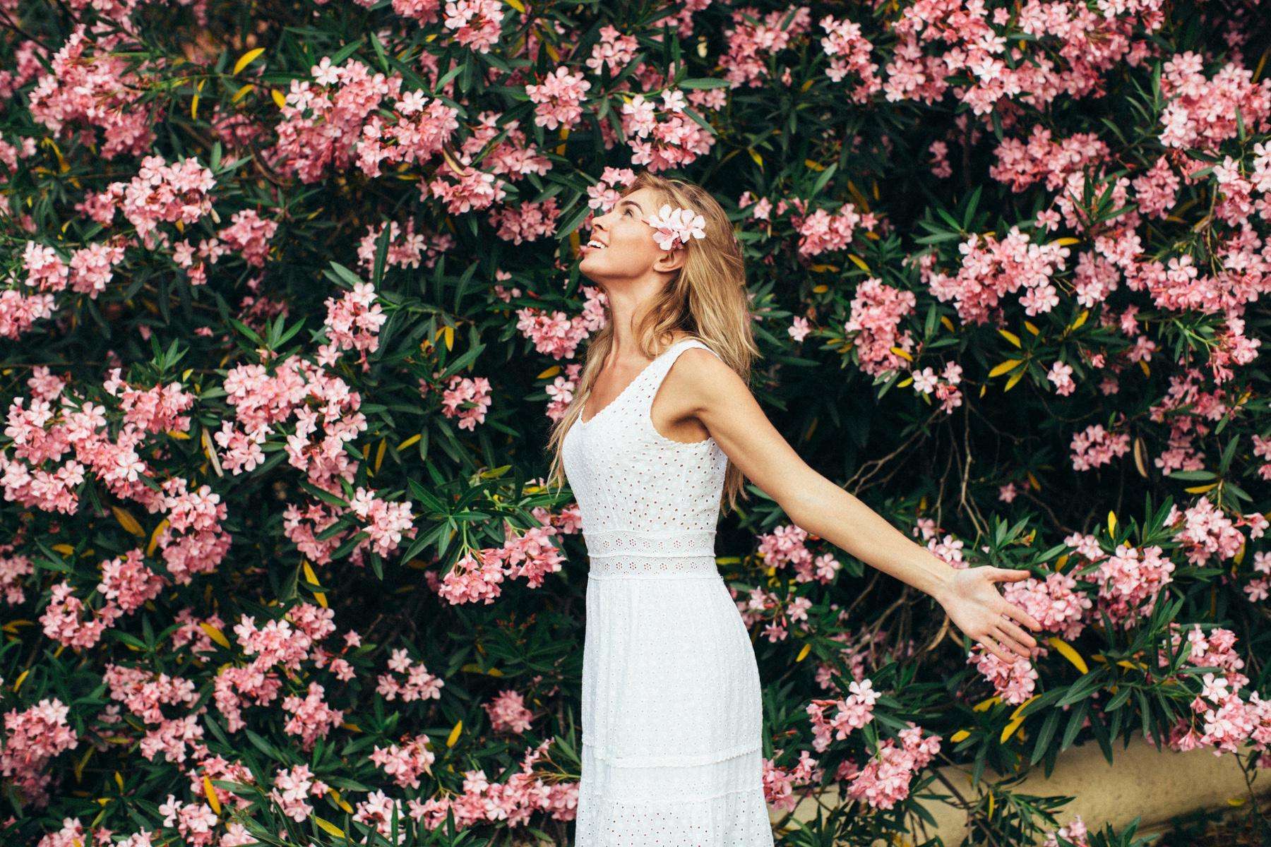 Woman standing next to a large bush with pink flowers.