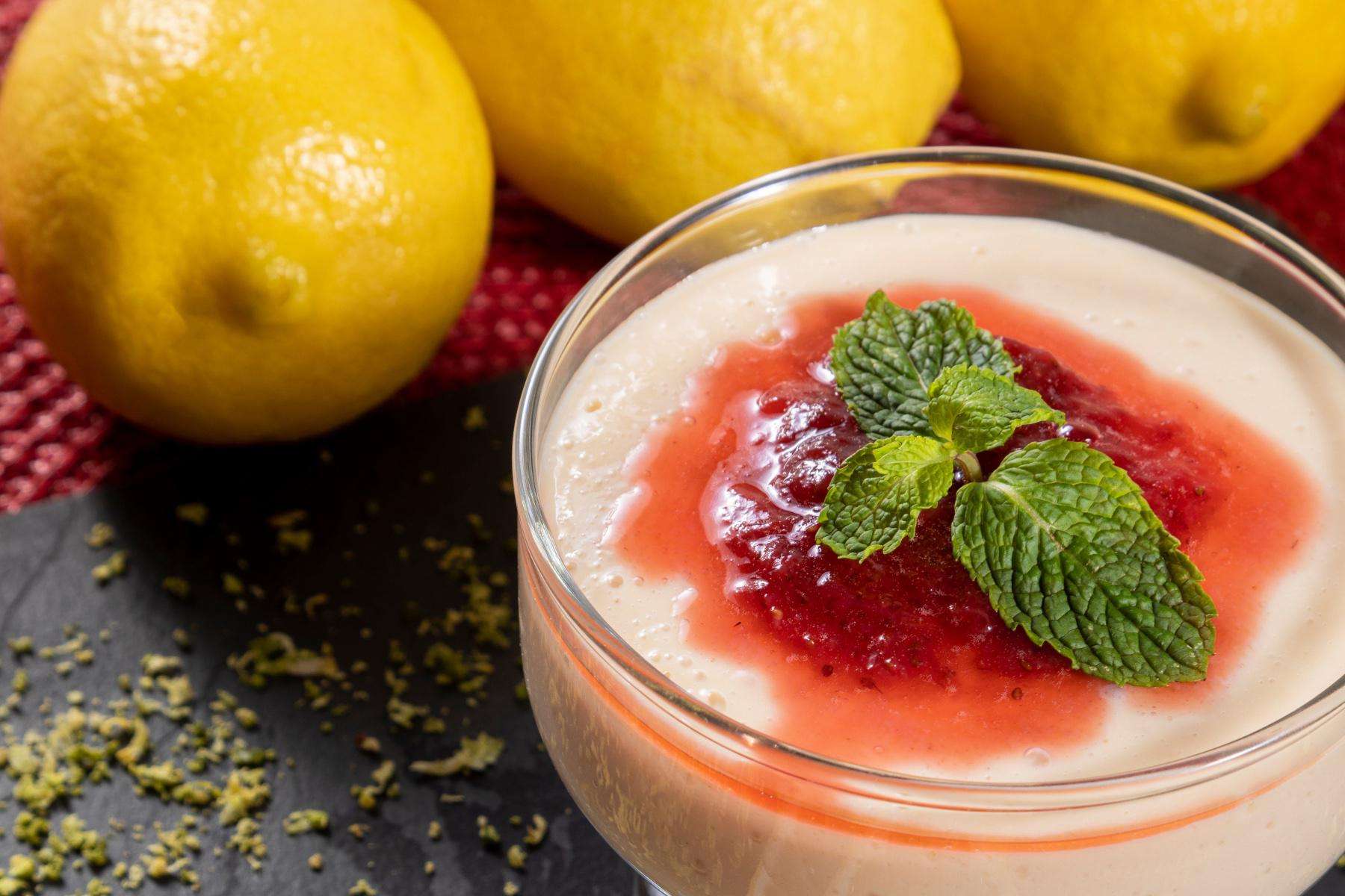 Close-up of lemon mousse in glass dish with lemons behind it.