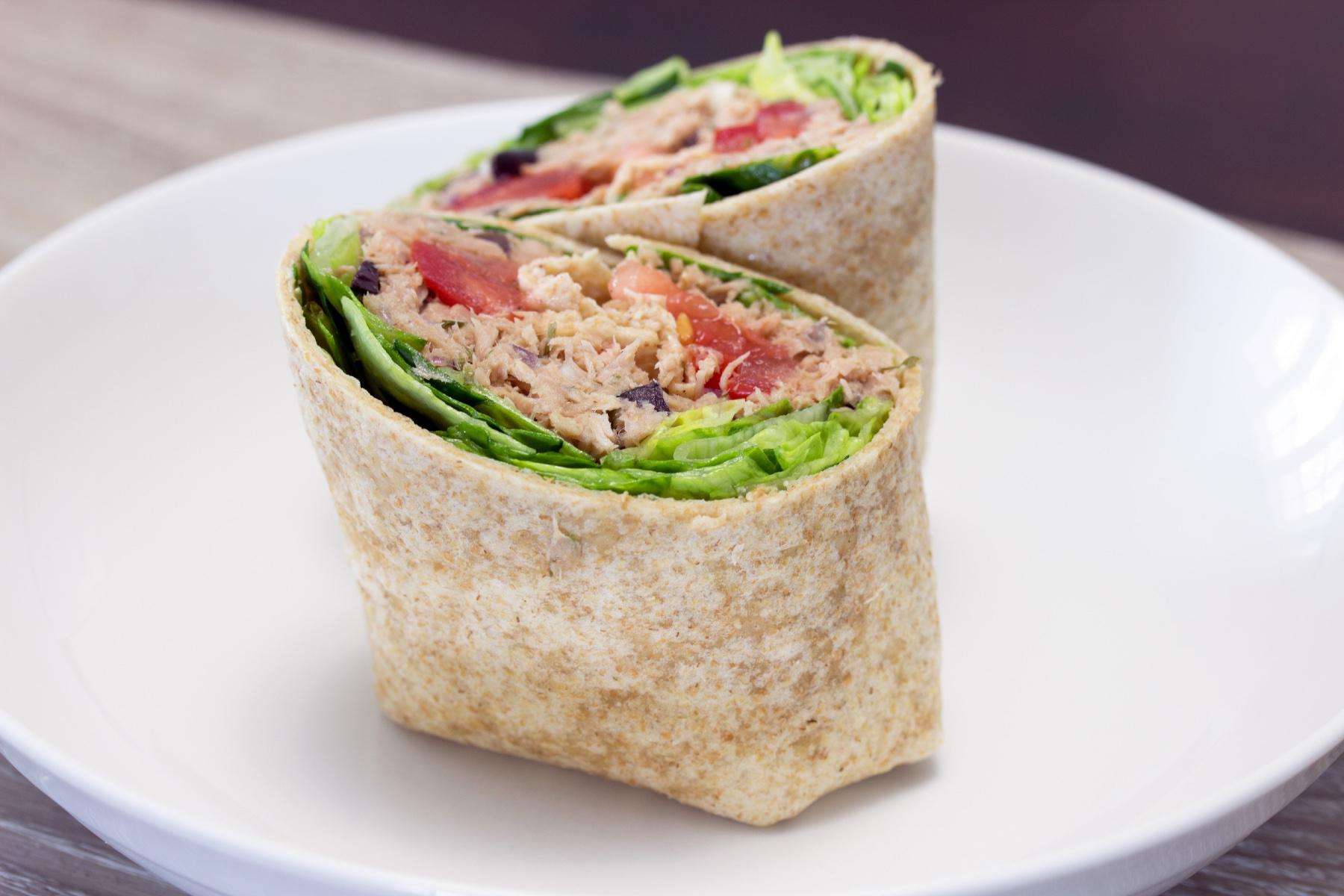 Close-up of a tuna salad wrap cut in half on a white plate.