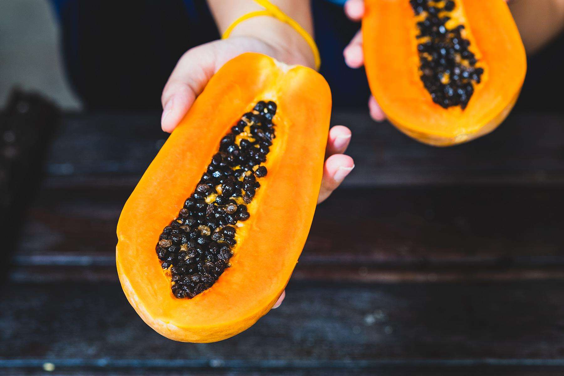 Hands holding a papaya cut in half.