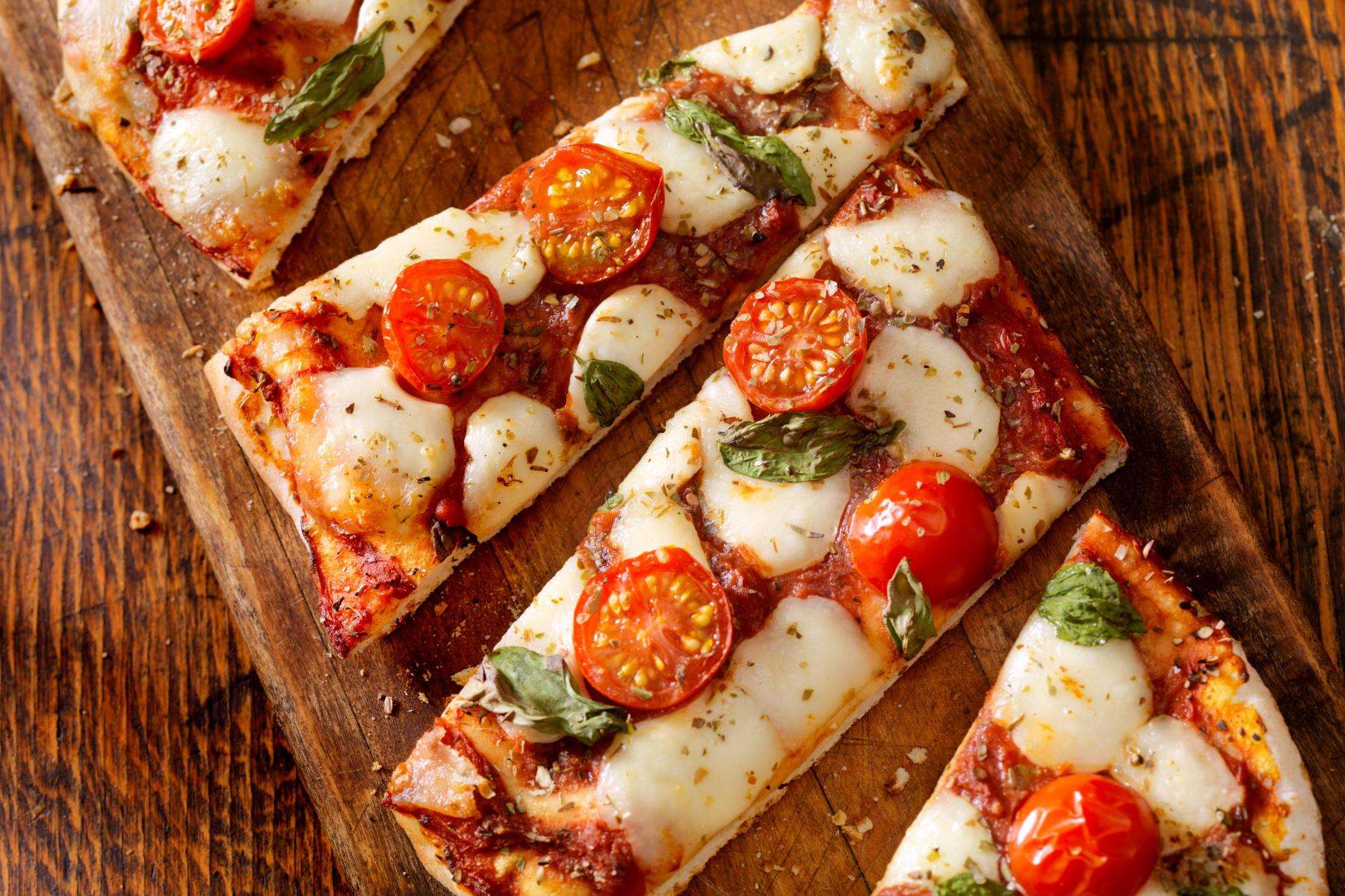 Overhead view of sliced Marguerite flatbread on wooden cutting board.