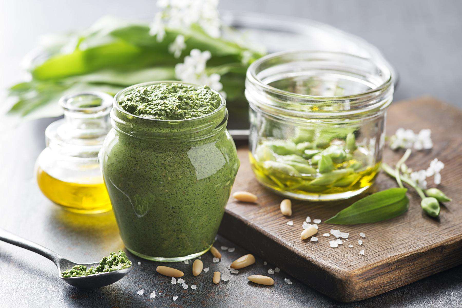 Close-up image of Basil Pine Nut Pesto in a jar with ingredients.