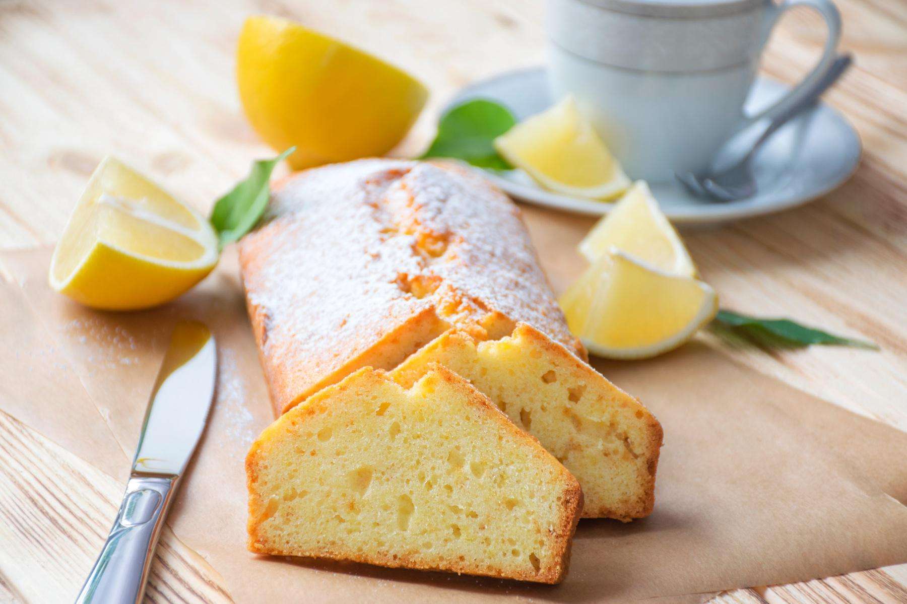 A loaf of lemon pound cake cut into slices on wooden cutting board.