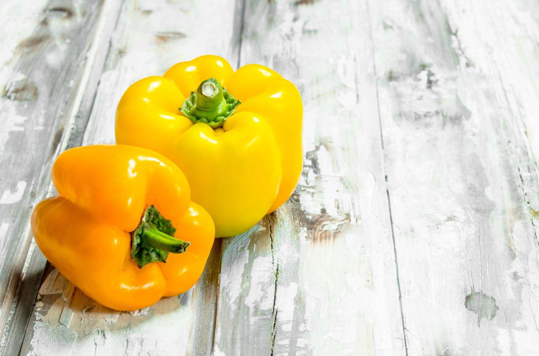 Two yellow bell peppers on a wooden table.