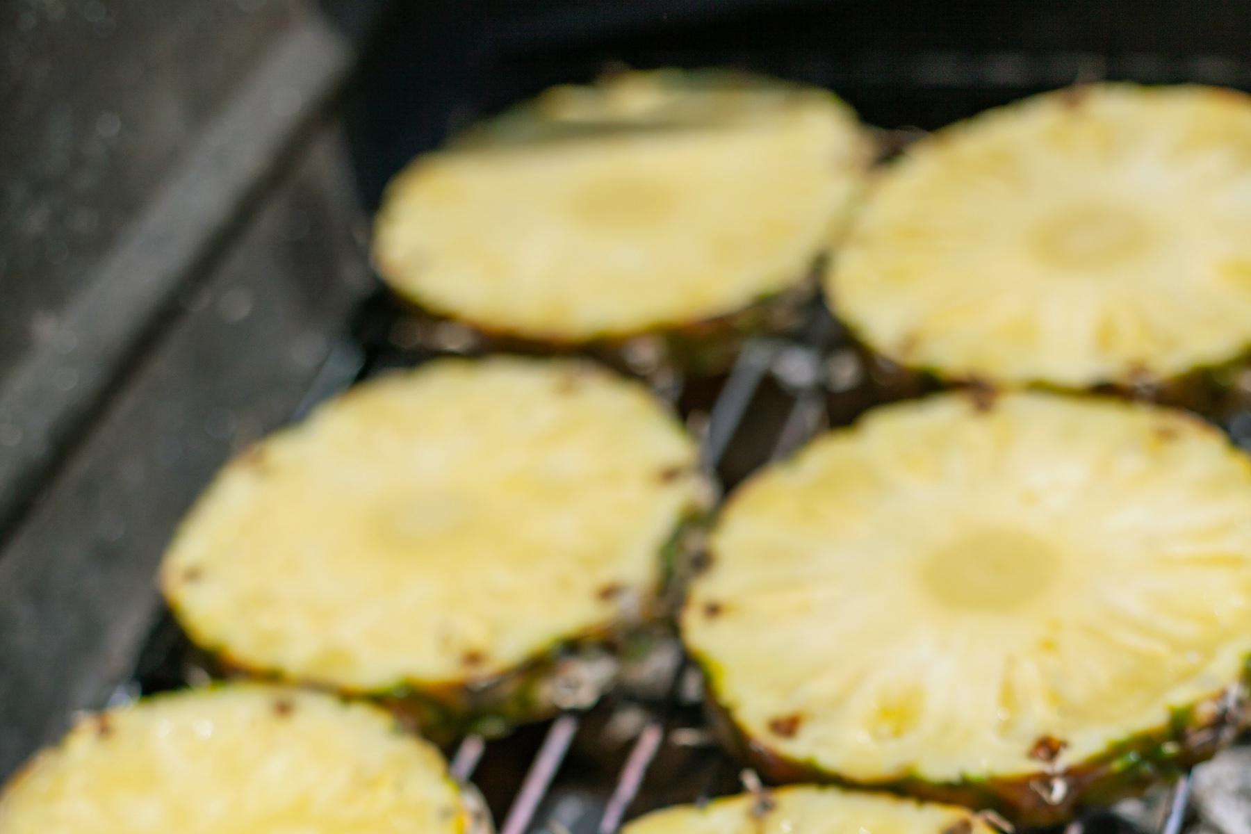 Slices of pineapple roasting on grill.