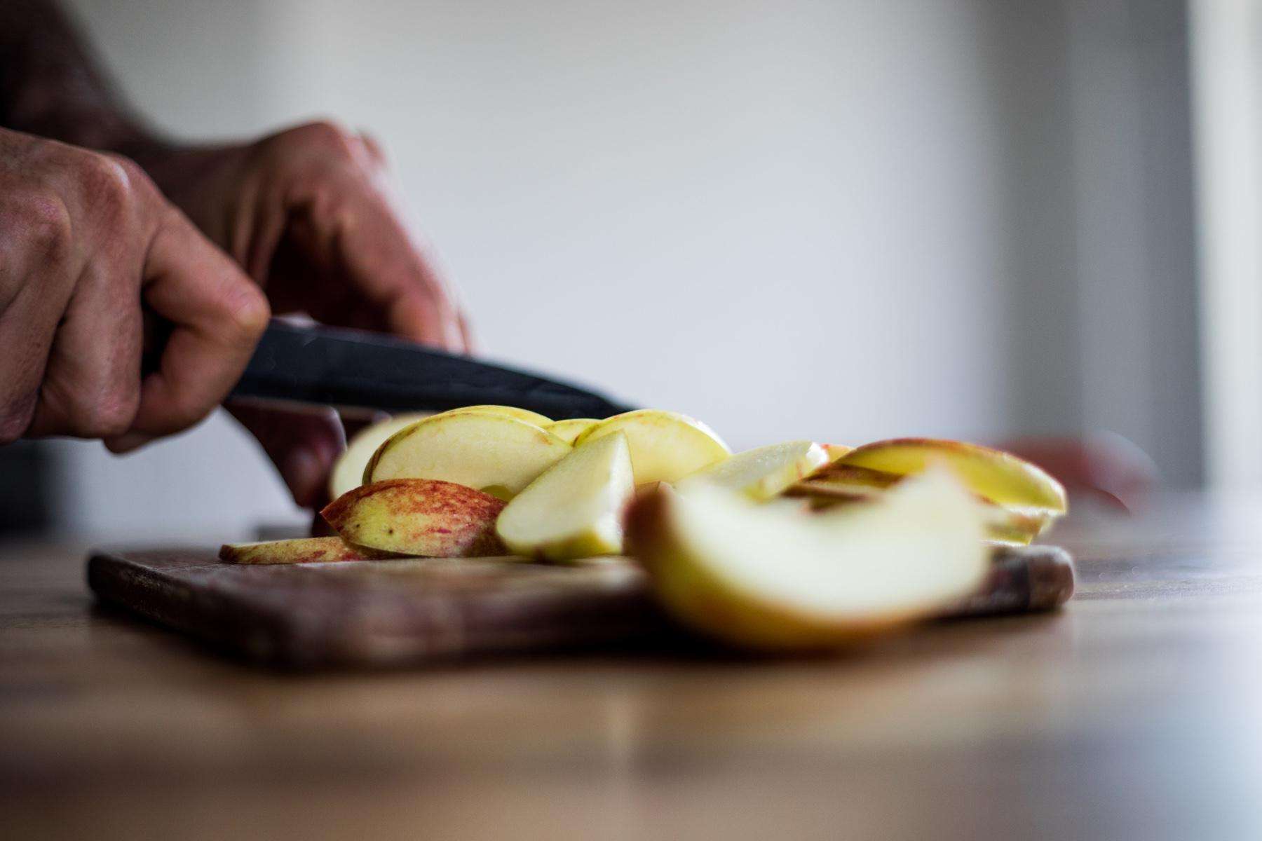 Close-up of hands chopping apple with knife from side.