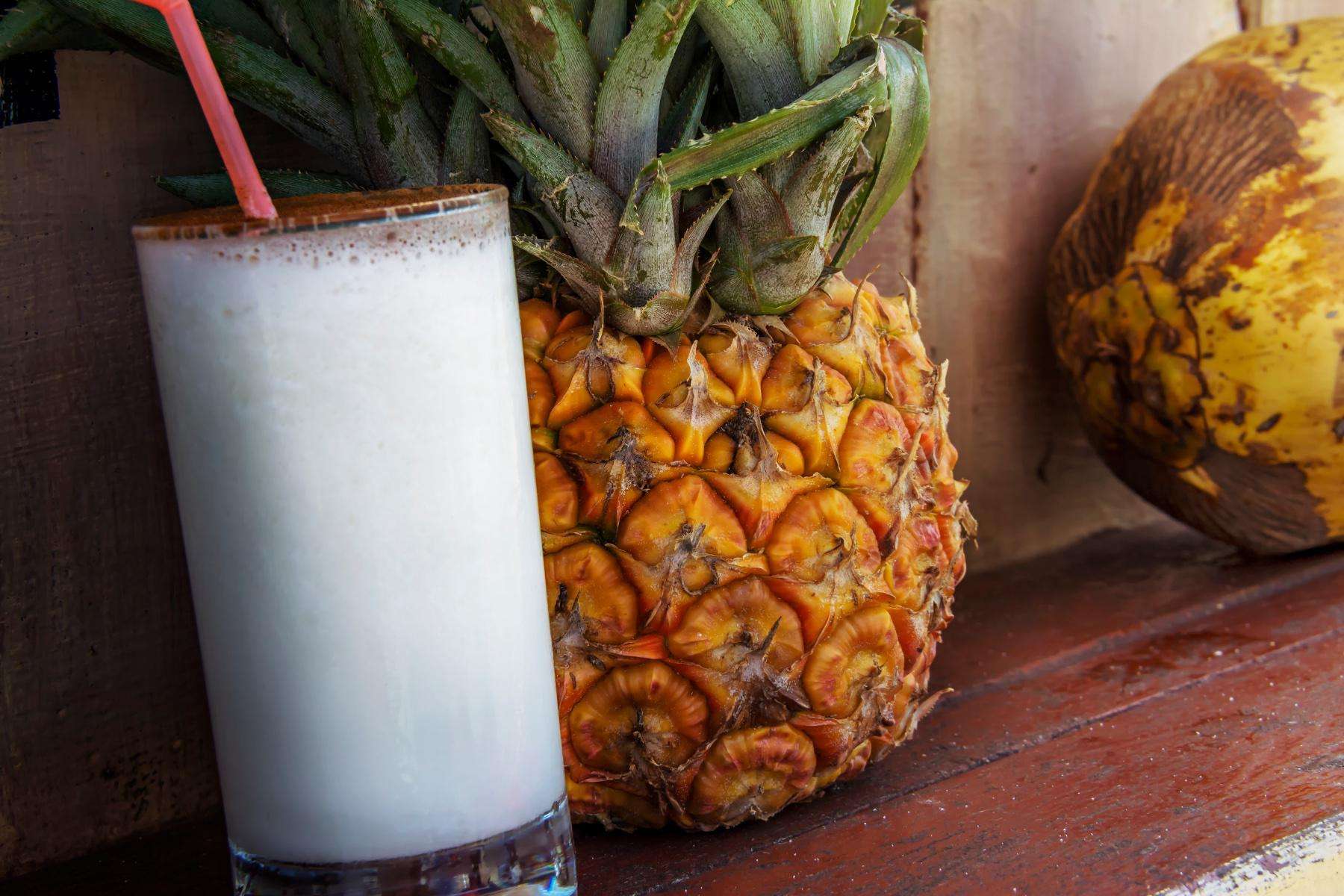 Pina colada smoothie in glass next to pineapple.