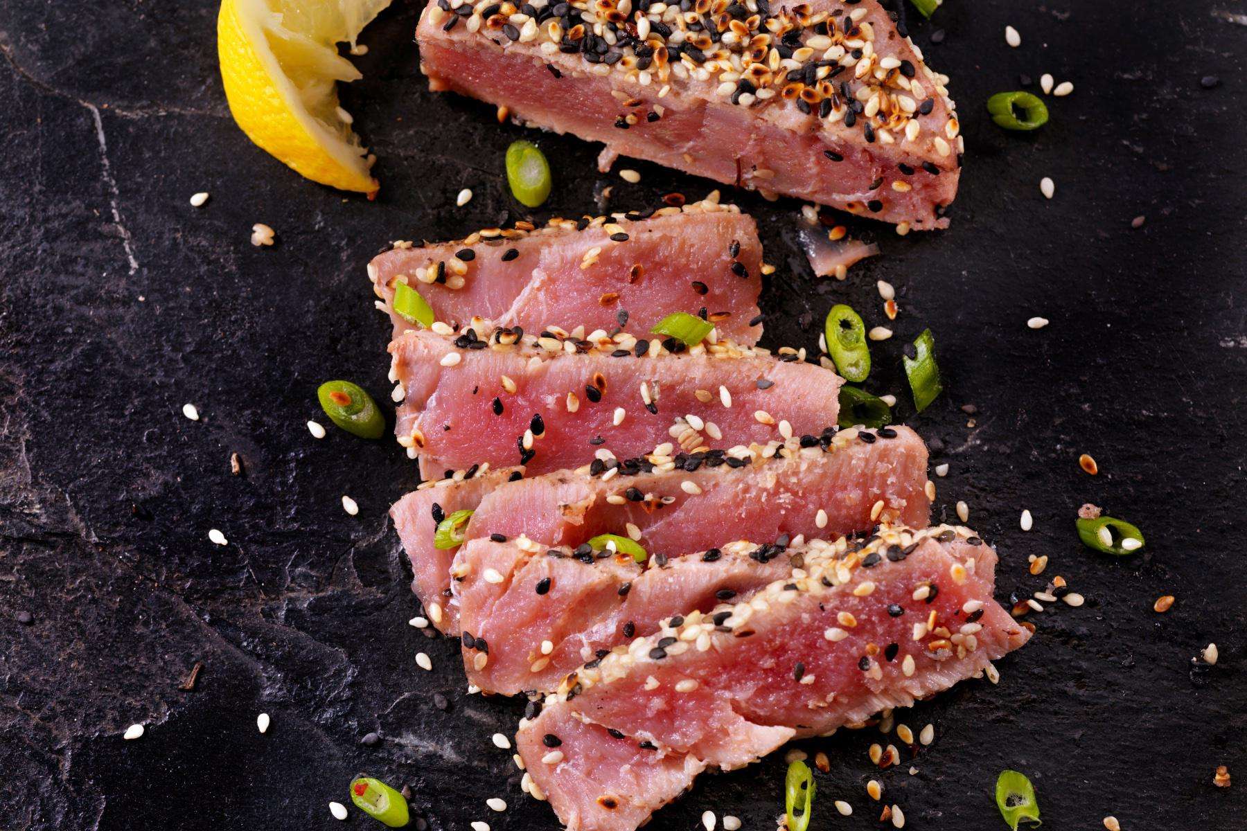 Slices of sesame crusted tuna on black plate.
