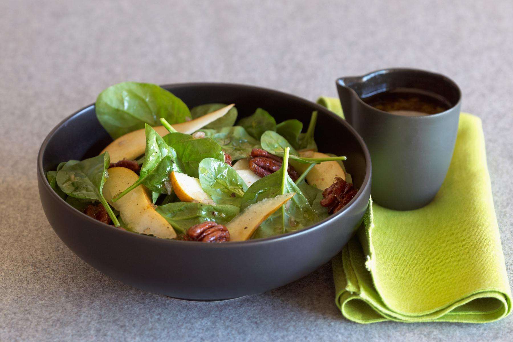 A black bowl filled with a spinach candied pecan salad and a cup of tea.