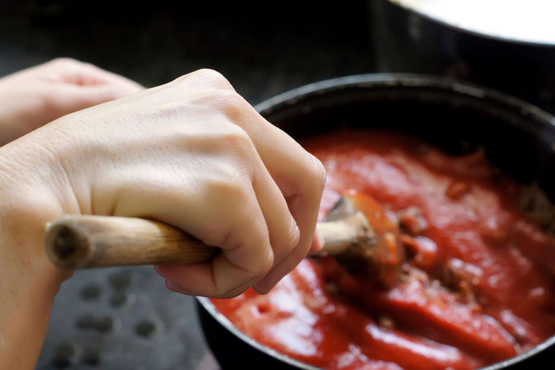 A woman stirring a plum tomato sauce on the stove.