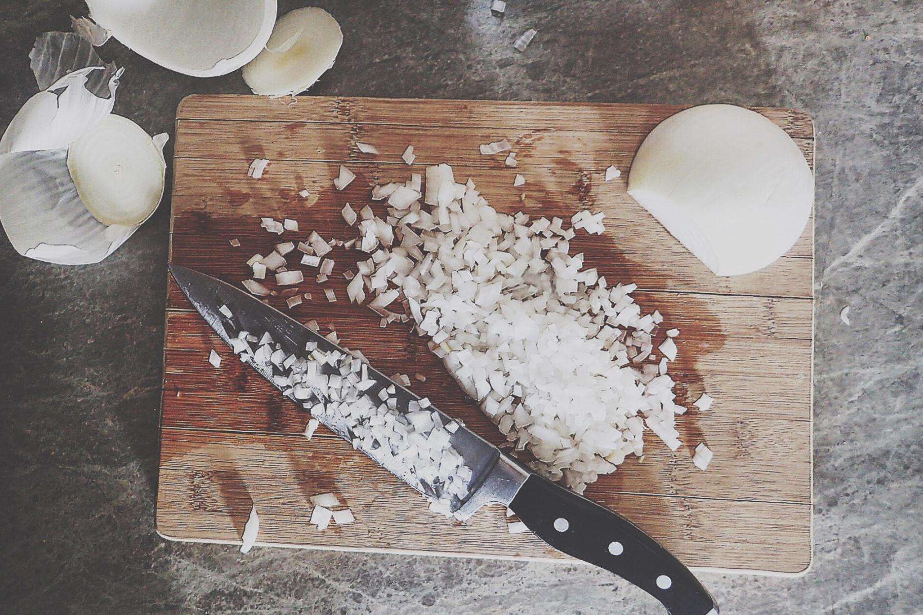Overhead view of onions chopped on wooden cutting board.