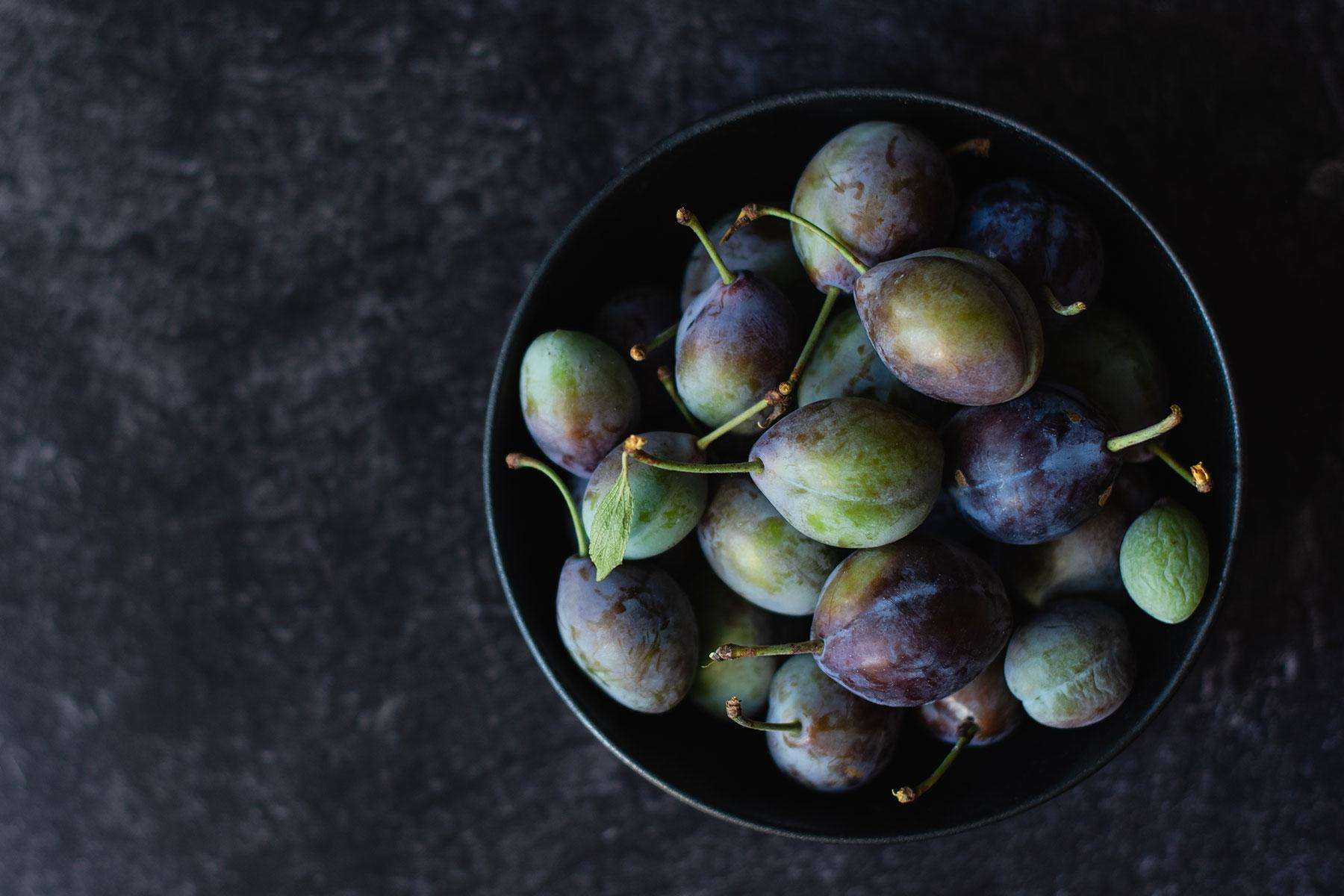 Bowl of fresh plums against dark background.
