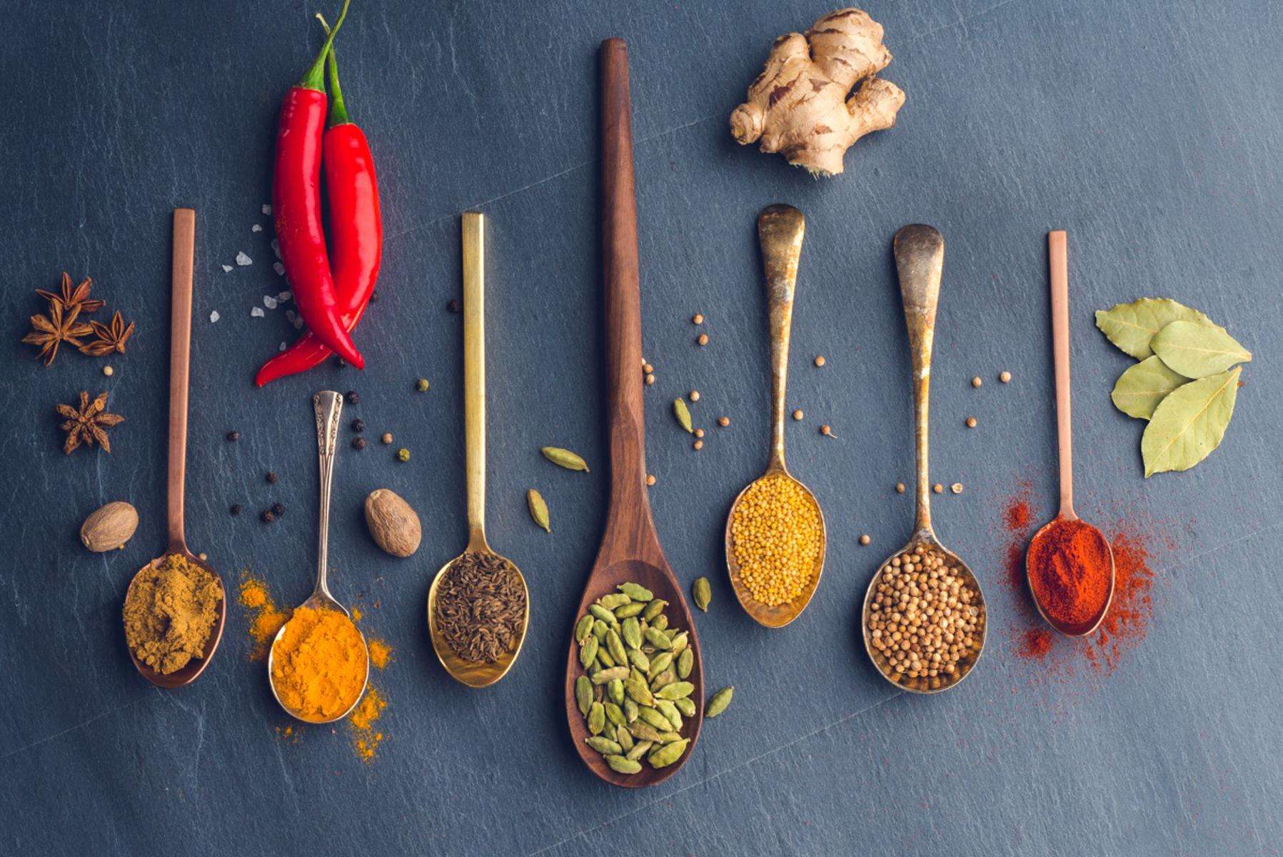 Overhead view of spices in wooden spoons on dark background.