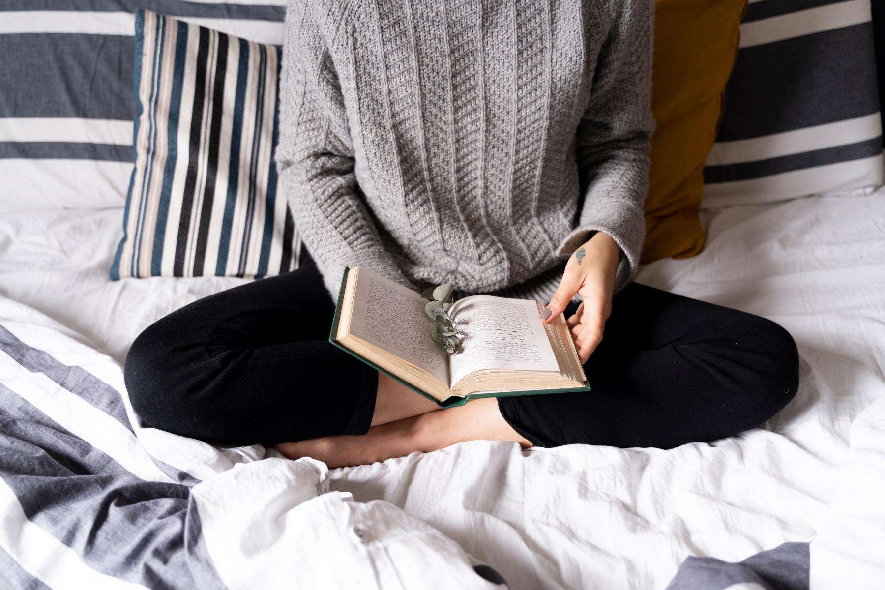 Overhead shot of woman reading book while sitting in bed.